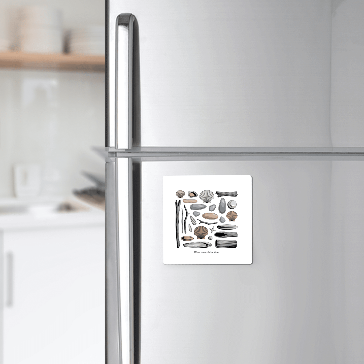 A silver fridge displays the Worn Smooth by Time Magnet – Coastal Driftwood & Shell Art from Mirabilia Boutique, a square beach magnet with seashell and stone illustrations—ideal ocean gift or sea glass decor for your kitchen.