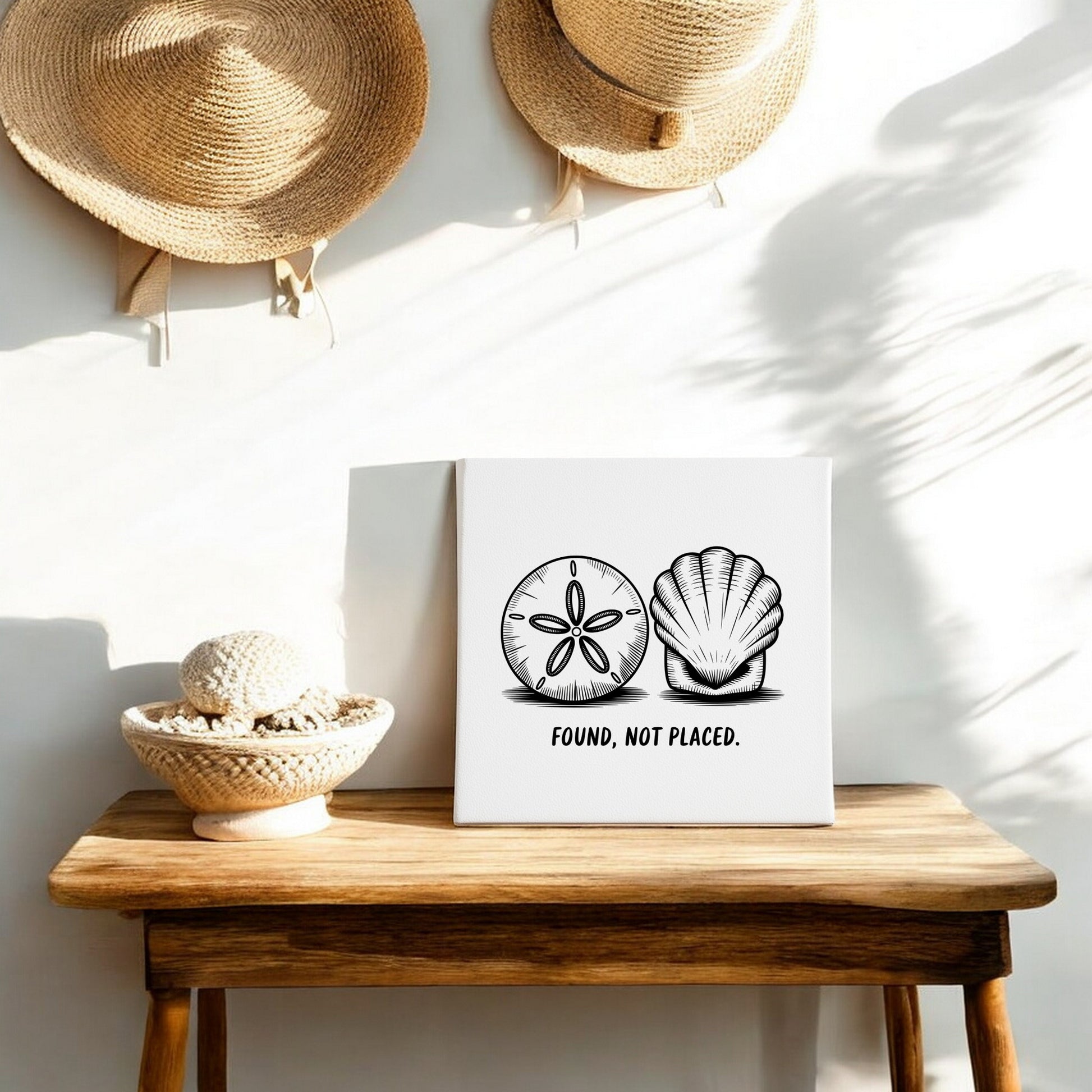 A wooden table displays the Found, Not Placed Canvas – Coastal Sketch Wall Art by Mirabilia Boutique. A basket with yarn and two straw hats complete this minimalist, beach-inspired scene in soft sunlight.