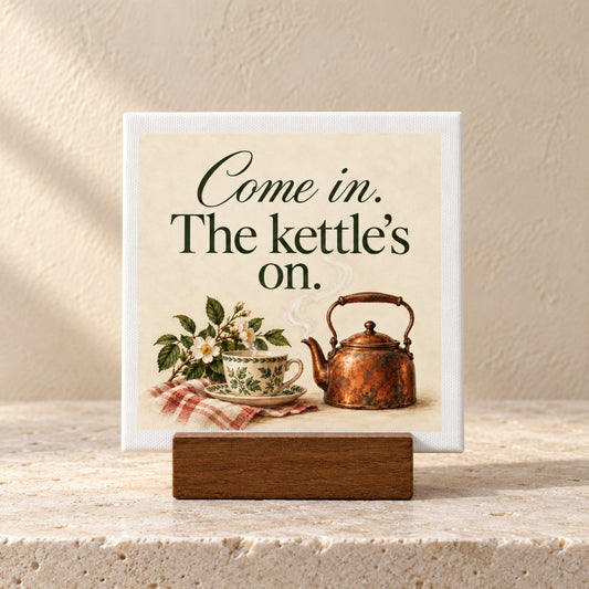 A Come In, The Kettle’s On Mini Canvas | Briar & Gable illustration on canvas featuring a steaming copper kettle, a teacup, and white flowers, with the text “Come in. The kettle’s on.” displayed on a small wooden stand.