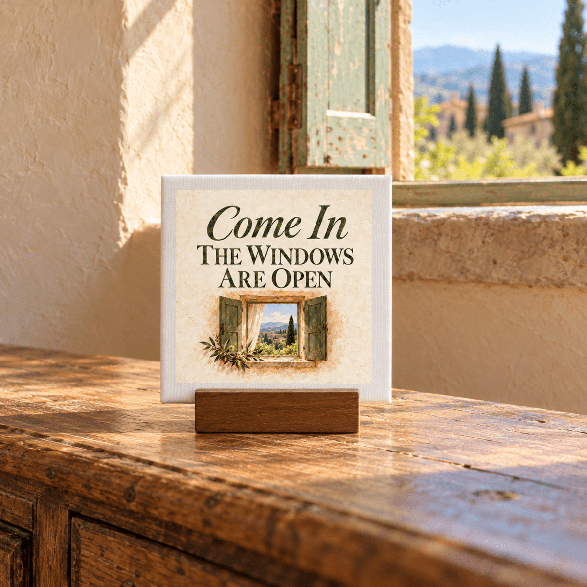 Come In Mini Canvas Sign | Ochre & Cypress on a wooden stand, featuring the text “Come In, The Windows Are Open” and an illustration of an open window overlooking a countryside landscape.