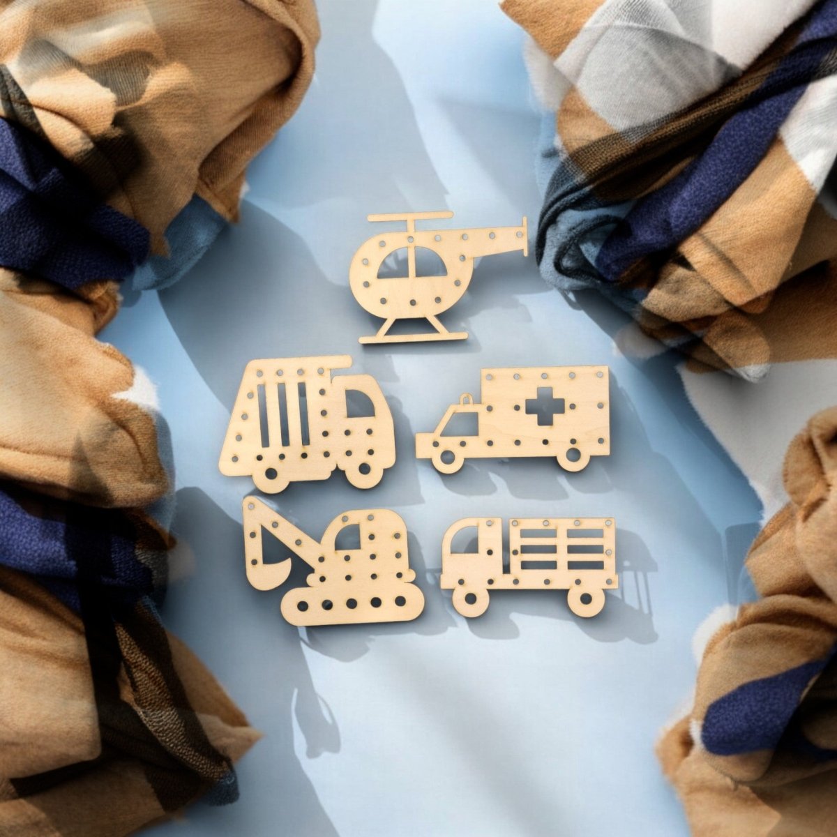 Mirabilia Boutique's Vehicle Lacing Trays for Fine Motor Skills feature wooden helicopter, garbage truck, ambulance, excavator, and fire truck cutouts on a blue surface with patterned fabric borders to boost motor development.