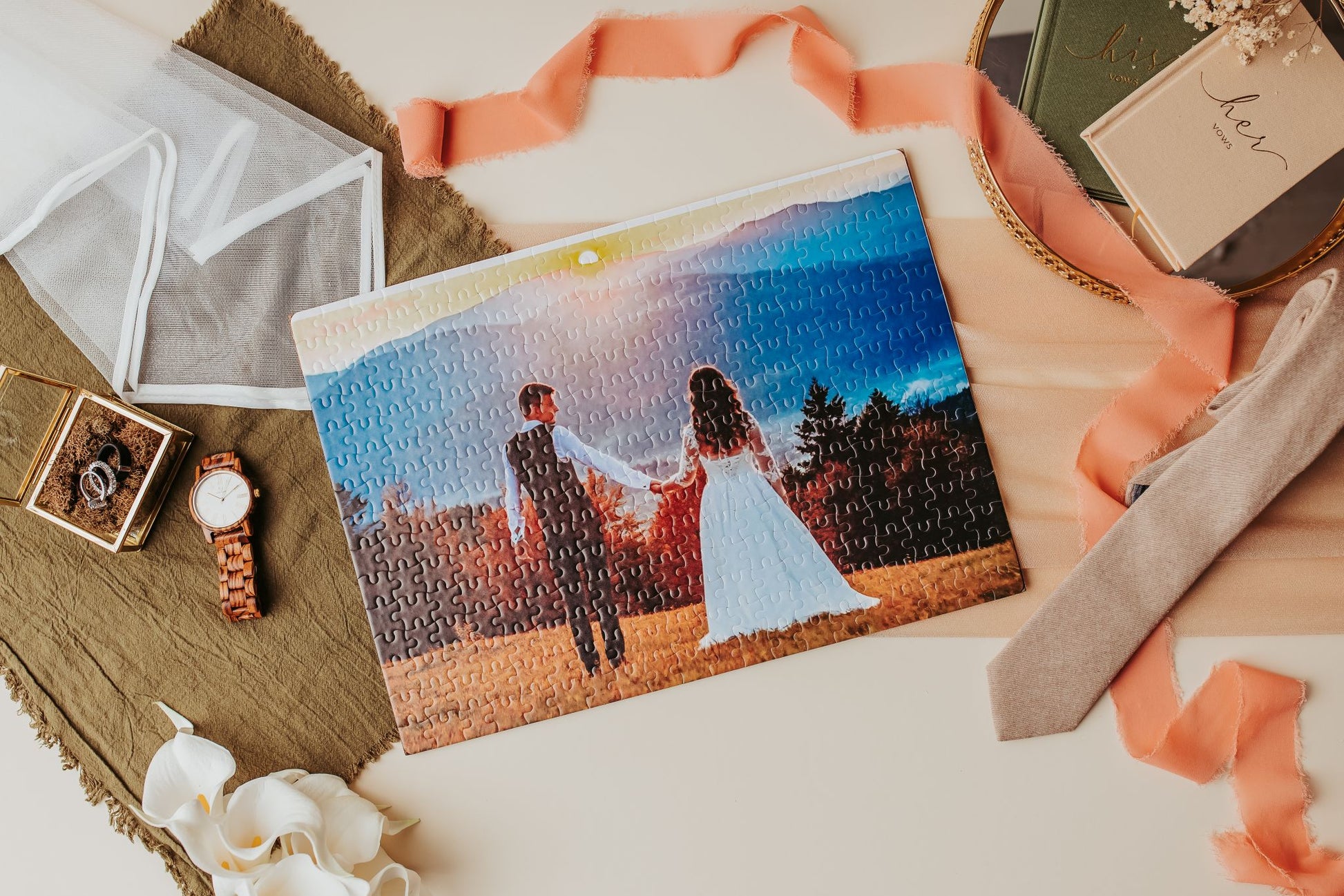 The Mirabilia Boutique Custom Wedding Jigsaw Puzzle | 300-Piece Photo Keepsake displays a bride and groom holding hands at sunset, with a watch, ring box, tie, ribbon, white flowers, and card on a tray.