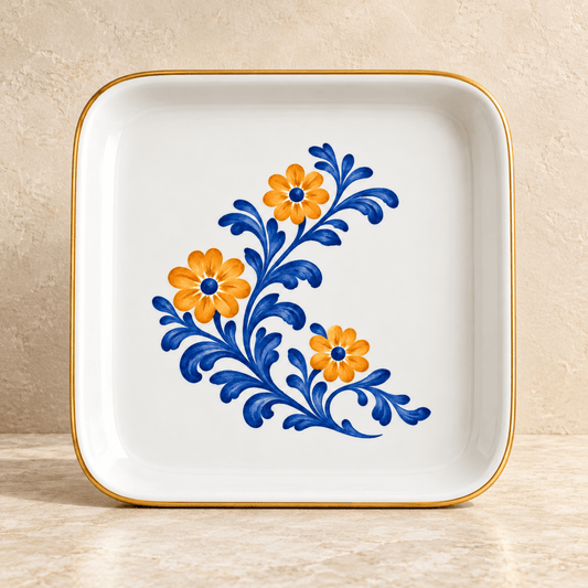 Courtyard Bloom Jewelry Tray, a square white ceramic tray with a gold rim and a painted floral motif of orange flowers and blue swirling leaves.