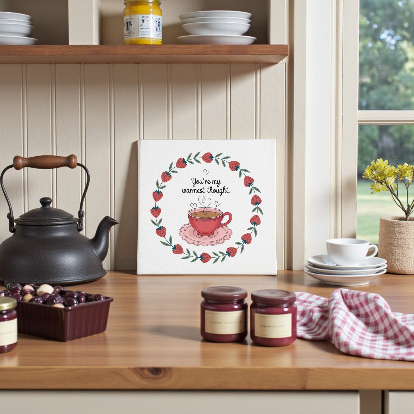 A cozy kitchen scene with the Mirabilia Boutique Warmest Thought Tea-Inspired Canvas Art, black teapot, cherries, jam jars, and checked towel—perfect as Valentine’s décor or a thoughtful tea lover gift on a wooden counter.