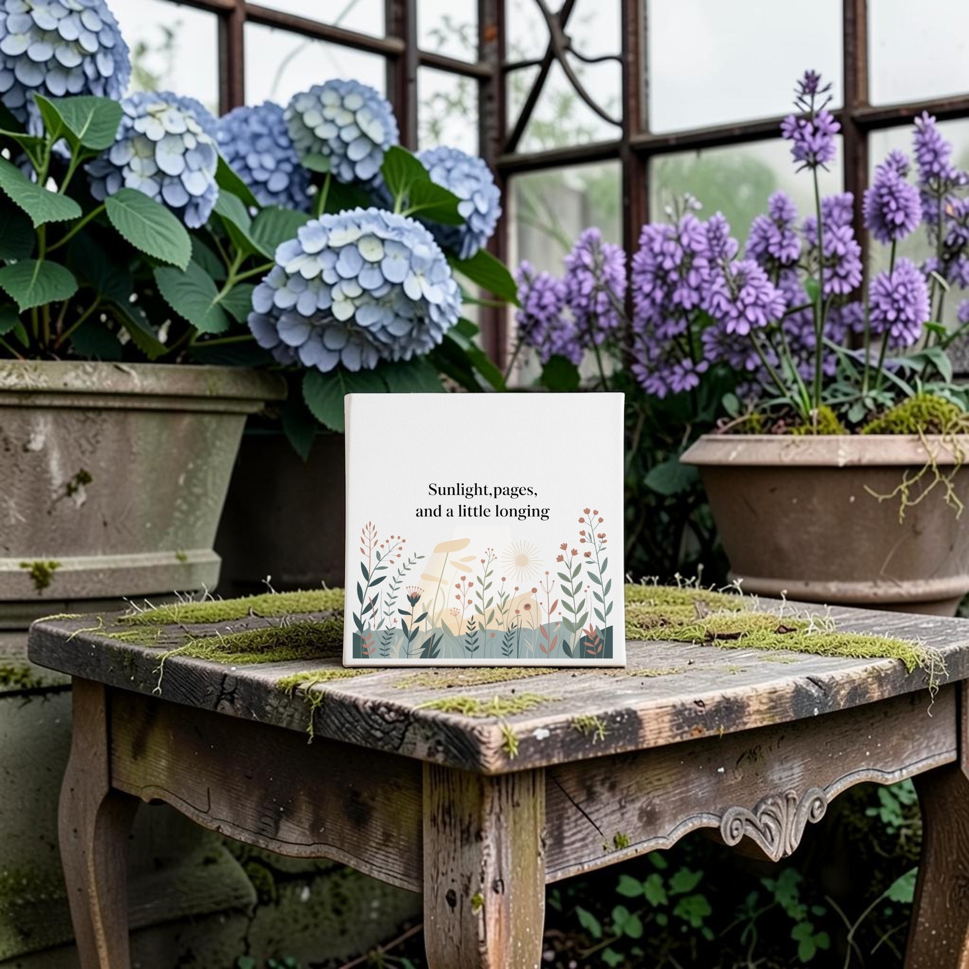 The Sunlight, Pages and a Little Longing Canvas by Mirabilia Boutique rests on a mossy table amid hydrangeas and botanical art in a greenhouse, adding dreamy literary charm to your home decor.