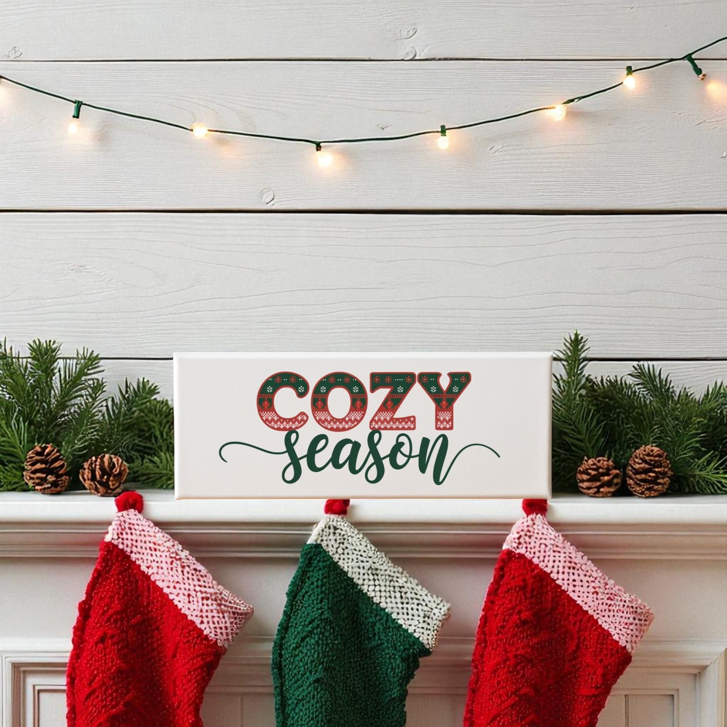 The Cozy Season Canvas Sign | 4x12 Holiday Wall Decor by Mirabilia Boutique rests on a mantel with pine branches and stockings, illuminated by string lights—a charming holiday accent for your home.