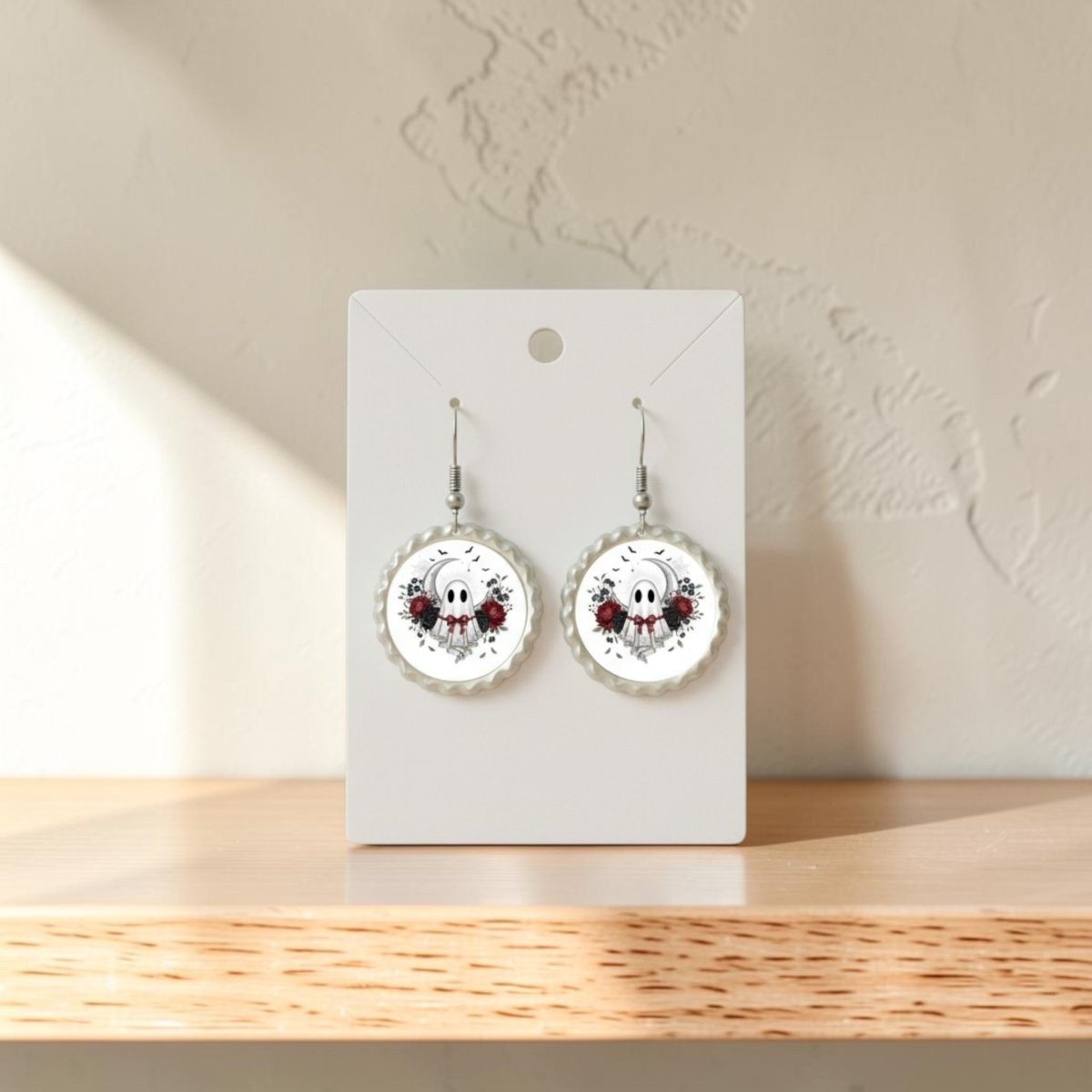 A pair of Crescent Moon Lace Ghost Scalloped Earrings from Mirabilia Boutique, displayed on a white card and set on a wooden surface with sunlight casting shadows, their vintage-inspired design evoking delicate charm.