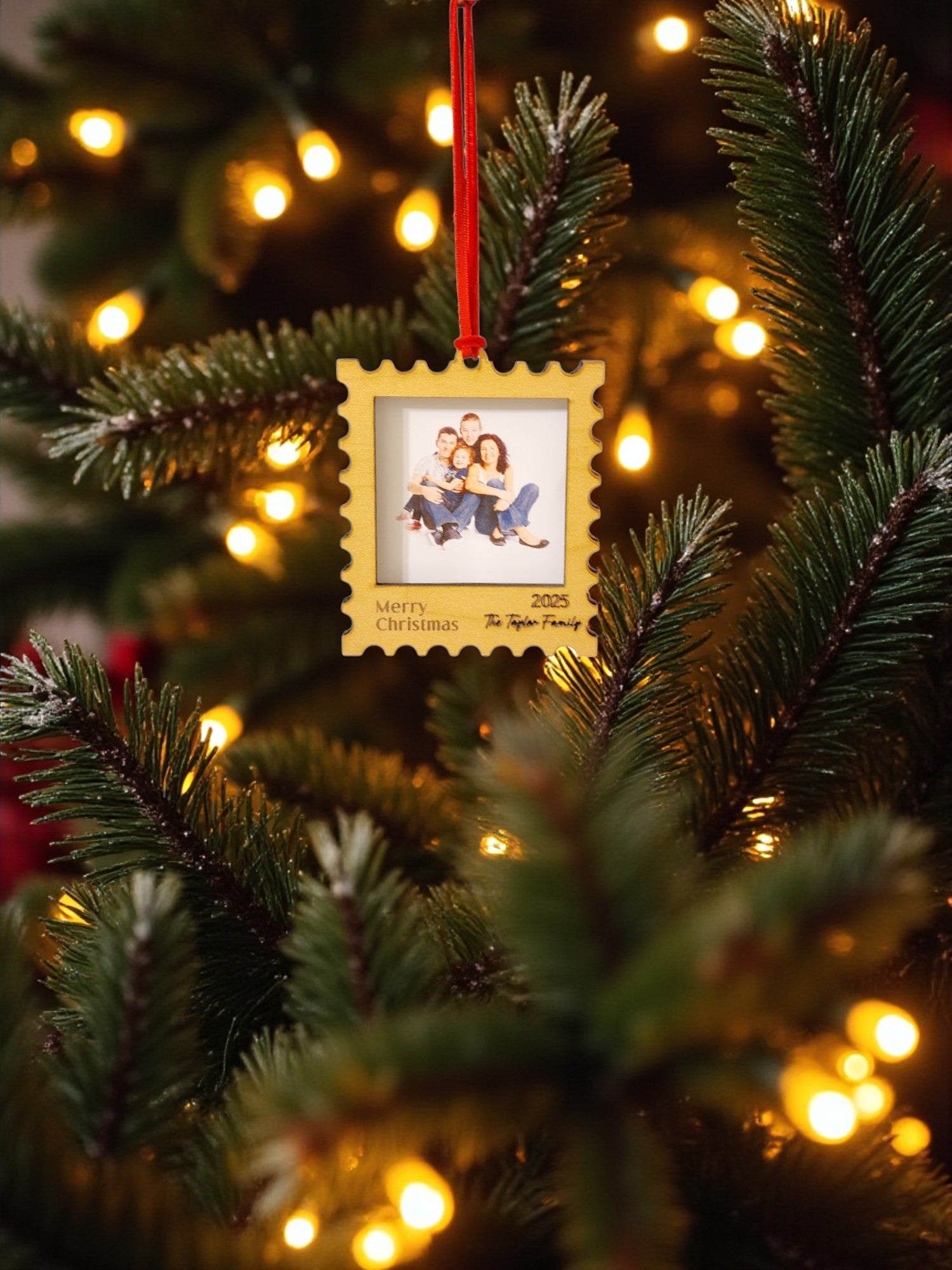A Christmas tree adorned with warm white lights and the Mirabilia Boutique Personalized Christmas Stamp Frame Ornament, custom-made with a smiling family photo and "Merry Christmas 2023 The Taylor Family.