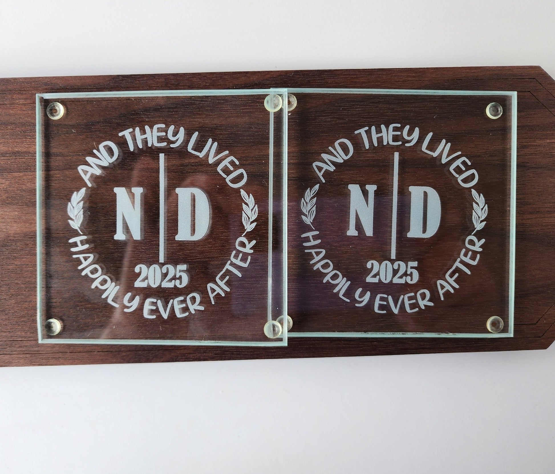The Personalized Glass Wedding Coasters by Mirabilia Boutique elegantly display "And They Lived Happily Ever After," featuring the initials "ND" and the year "2025," making a unique and perfect personalized wedding gift.