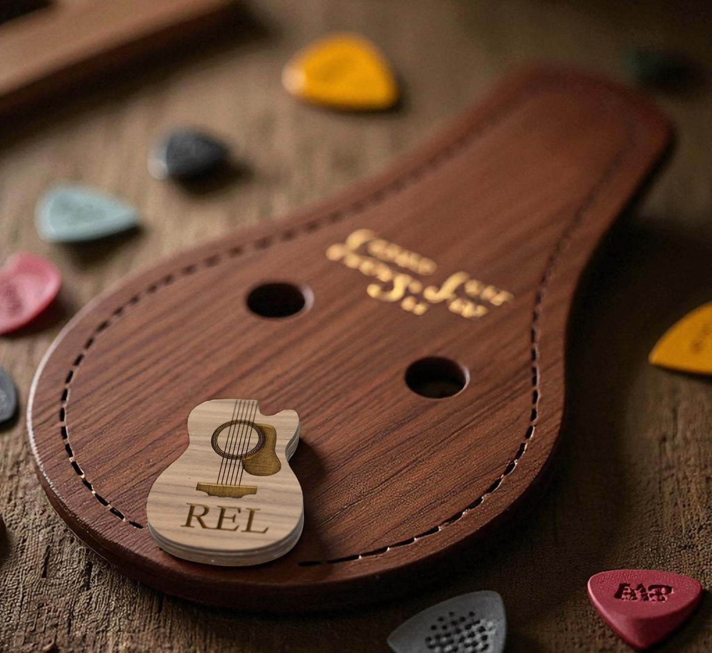 The Mirabilia Boutique Custom Guitar Pick Box, a personalized music gift for guitarists, features a guitar-shaped wooden holder with "REL" engraving and pick slots, displayed with colorful picks—an ideal gift on any wooden surface.