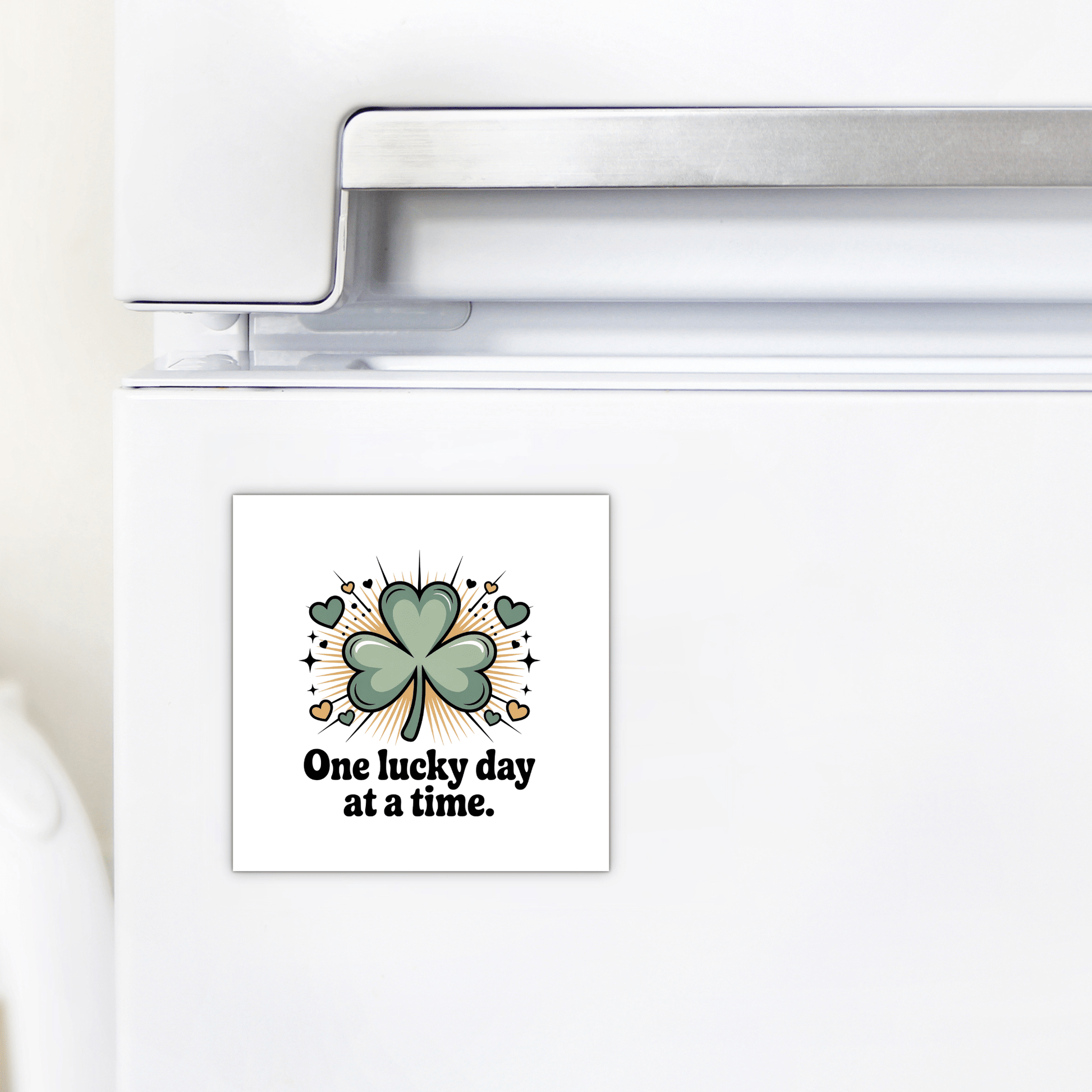 A white refrigerator features the Mirabilia Boutique "One Lucky Day at a Time Magnet," decorated with a green four-leaf clover, small hearts, sparkles, and the phrase "One lucky day at a time.