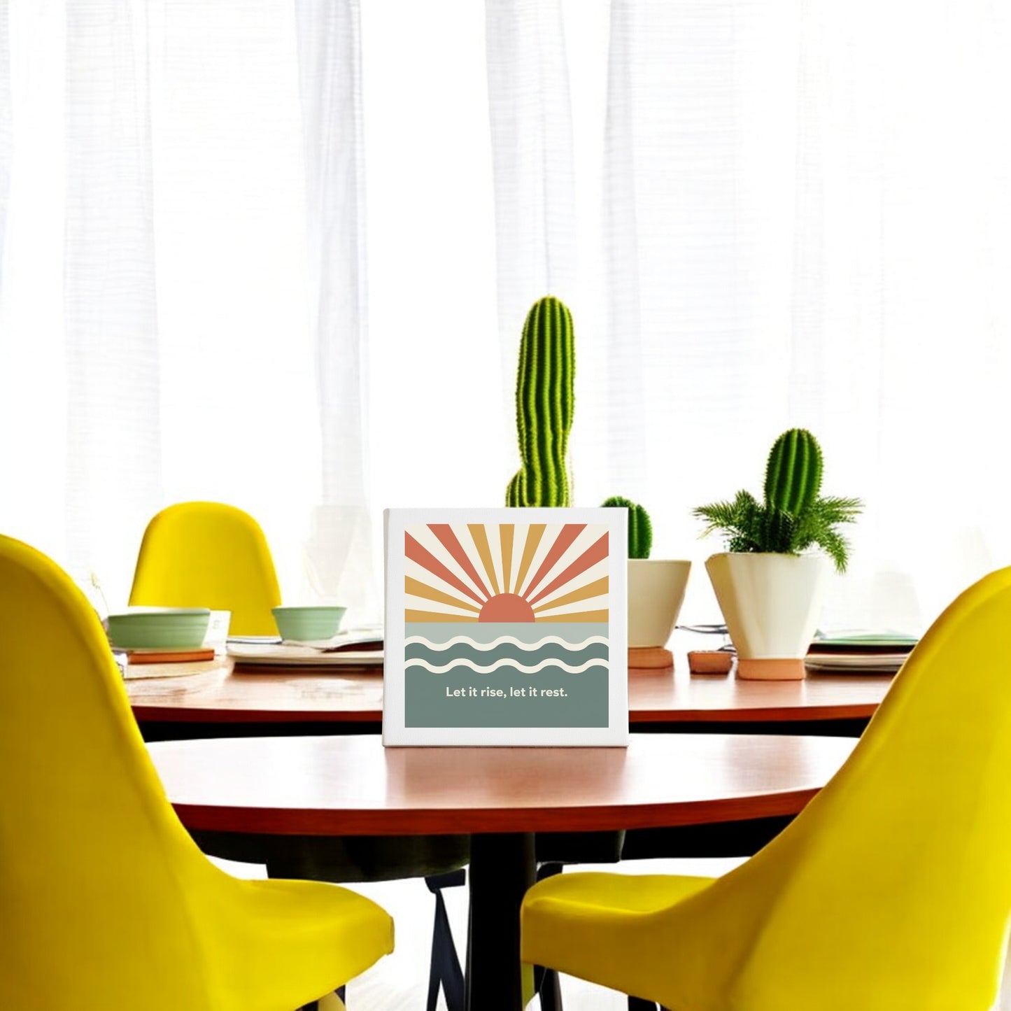 A round dining table with yellow chairs and potted cacti centers the "Let It Rise, Let It Rest Canvas – Sunrise Mindful Art" by Mirabilia Boutique. Sheer white curtains hang in the background.