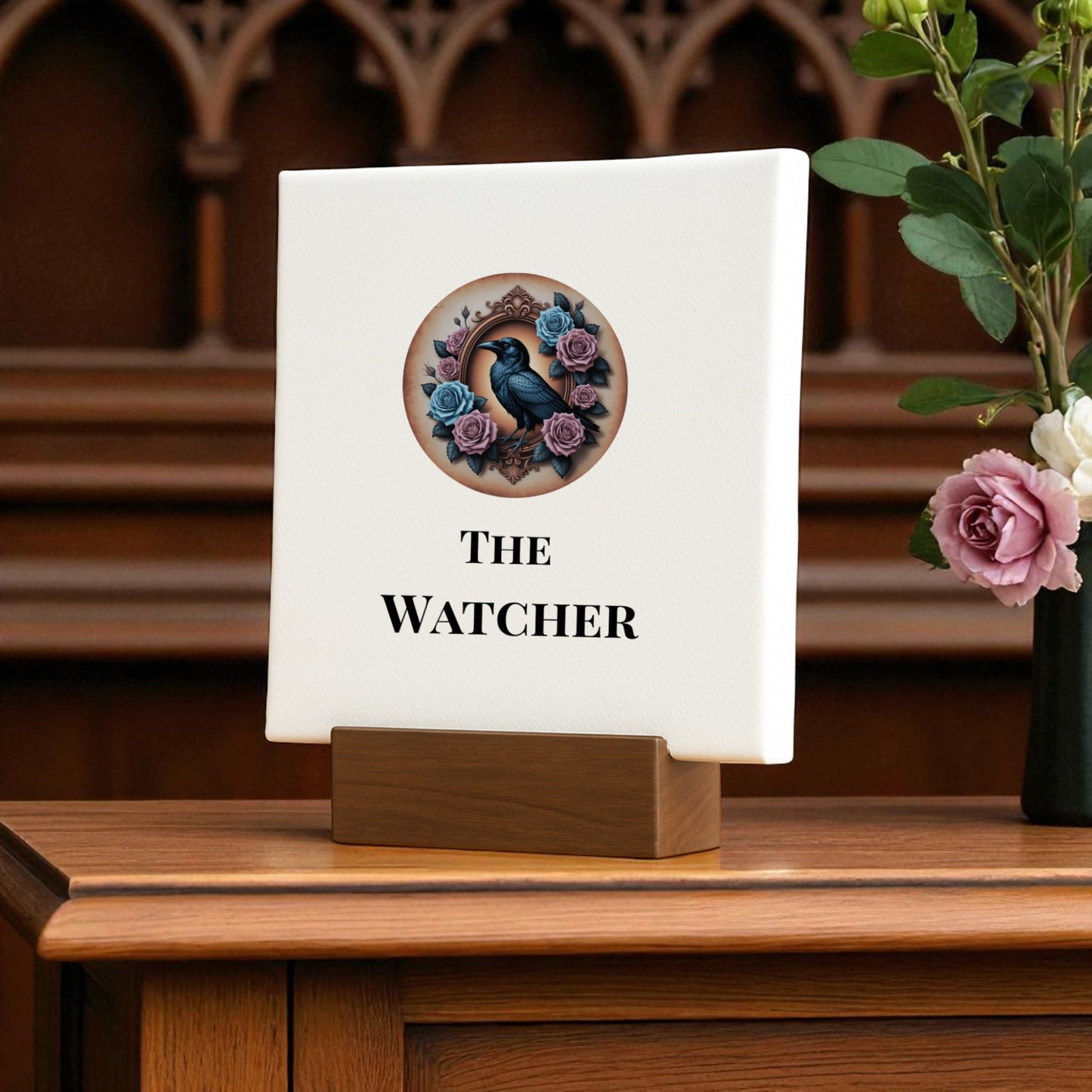 The Mini Gothic Sign | The Watcher by Mirabilia Boutique features a raven surrounded by purple and pink roses atop a wooden stand, with "The Watcher" inscribed and a pink rose with greenery accenting the right side. Perfect gothic décor.