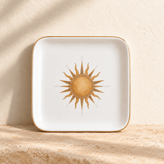 The Desert Sun Jewelry Tray | Sage & Stone by Mirabilia Boutique is a white tray with a gold-colored rim and sun illustration, displayed on a textured beige surface against a matching wall.
