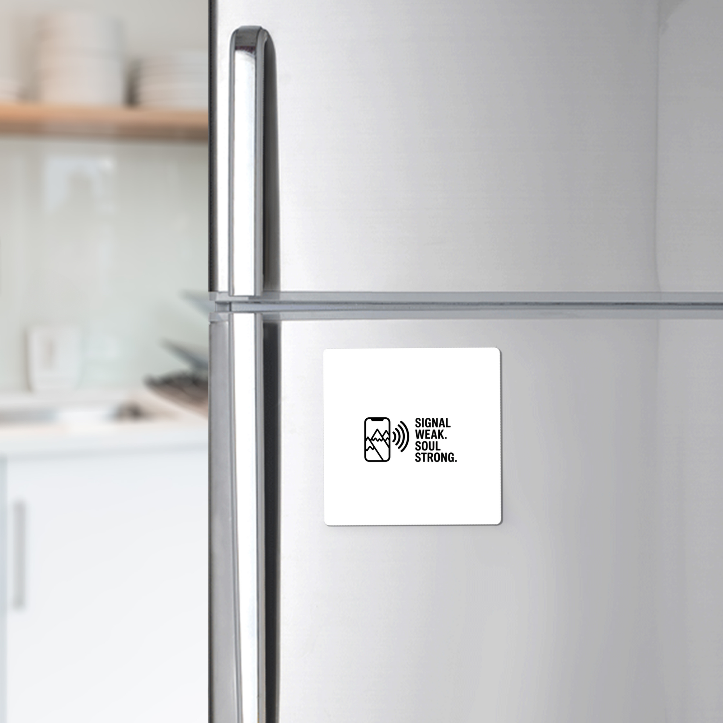 A silver refrigerator displays the Mirabilia Boutique Signal Weak Soul Strong Adventure Magnet, a white square featuring a signal icon and "SIGNAL WEAK. SOUL STRONG." in black. White dishes sit on a shelf in the background.