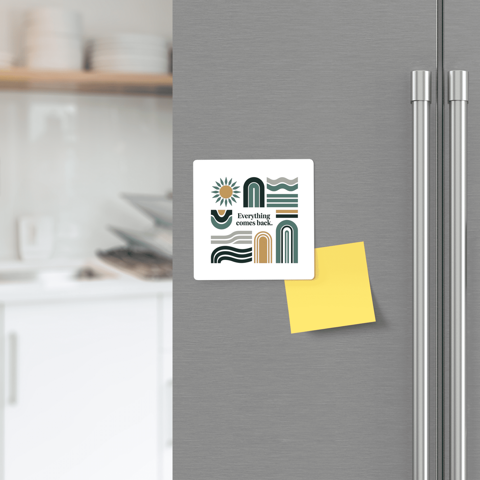 A refrigerator door displays Mirabilia Boutique's "Everything Comes Back" Earth Tone Affirmation Magnet—mid-century modern abstract design—mounted above a yellow sticky note, with a softly blurred kitchen in the background.