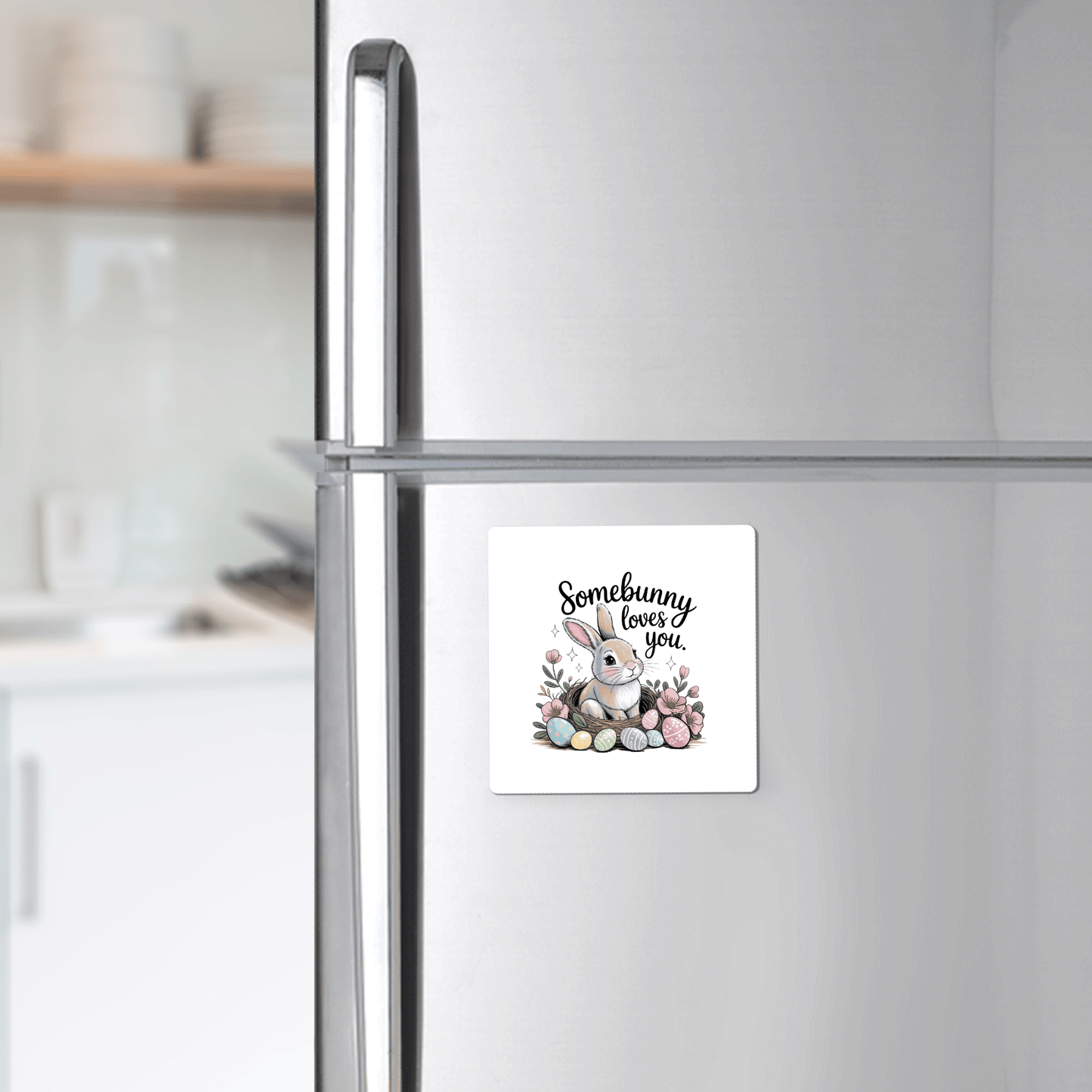 The Somebunny Loves You Magnet from Mirabilia Boutique features a bunny with flowers and eggs and the phrase “Somebunny loves you,” adding cute spring decor to your kitchen fridge. A blurred kitchen background enhances its charm.