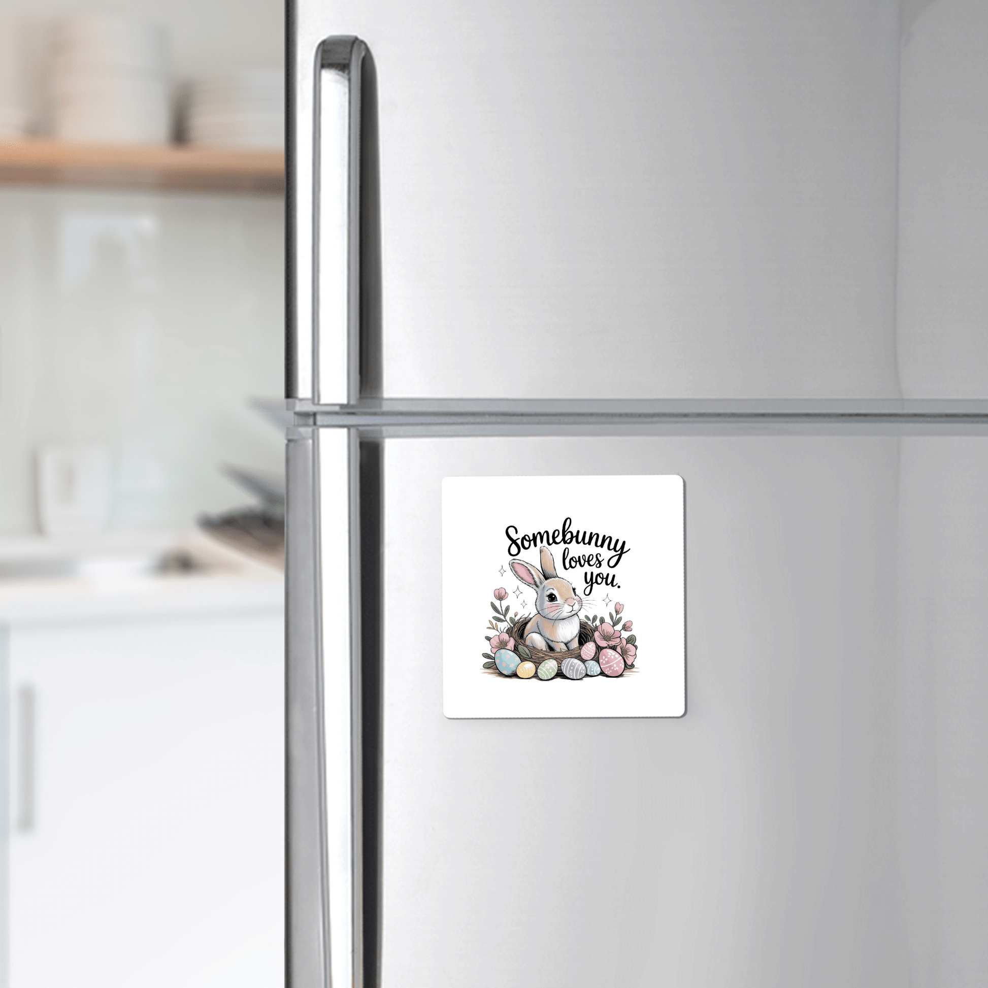 The Somebunny Loves You Magnet from Mirabilia Boutique features a bunny with flowers and eggs and the phrase “Somebunny loves you,” adding cute spring decor to your kitchen fridge. A blurred kitchen background enhances its charm.