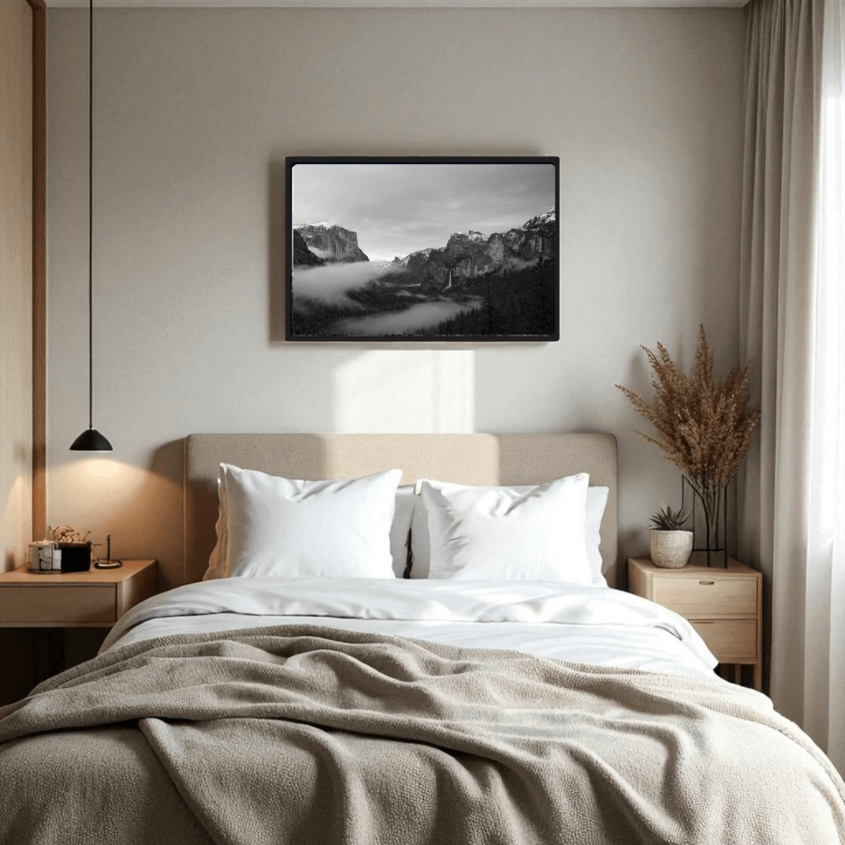 A cozy bedroom featuring a beige upholstered bed, white bedding, wooden side tables, and a black pendant lamp. Above the bed hangs the Yosemite Valley Black & White Fine Art framed print by Mirabilia Boutique. Dried plants sit on the right side table.