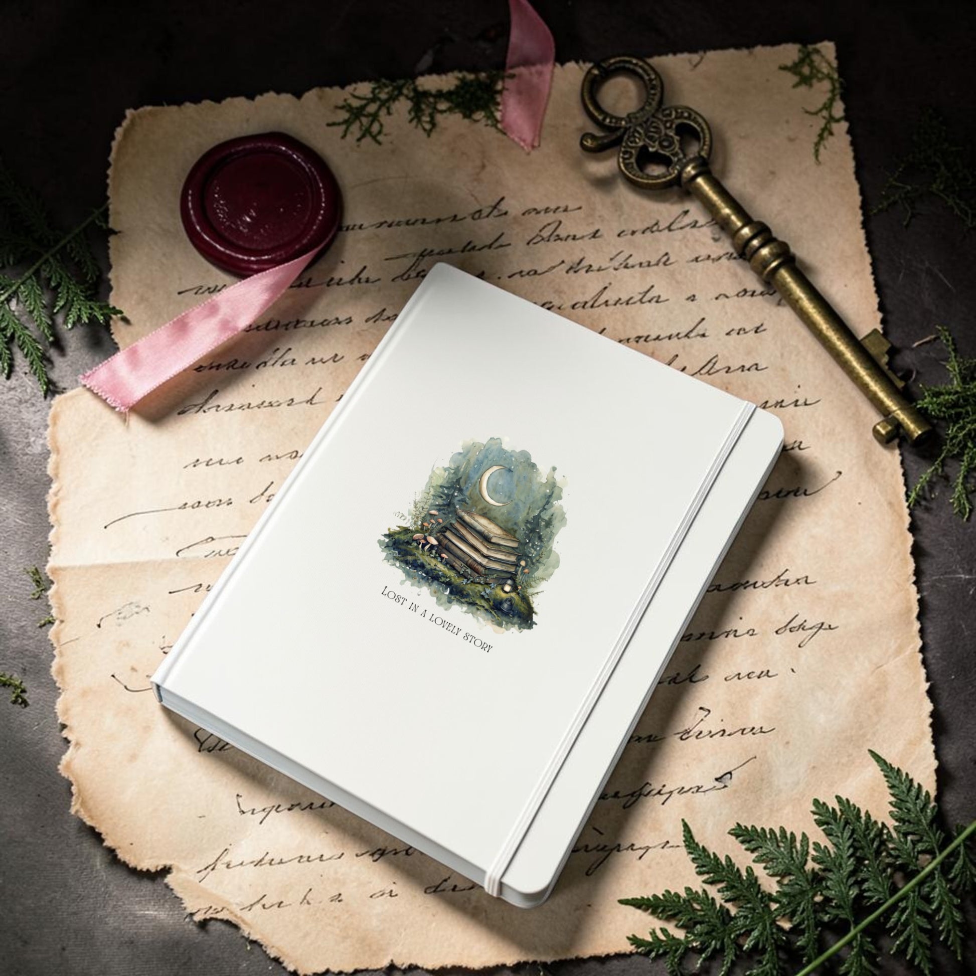 The Lost in a Lovely Story Journal by Mirabilia Boutique—a white hardcover adorned with a moon and book illustration—rests atop an old handwritten letter, accompanied by a vintage key, a wax seal tied with a pink ribbon, and fern leaves against a dark background.