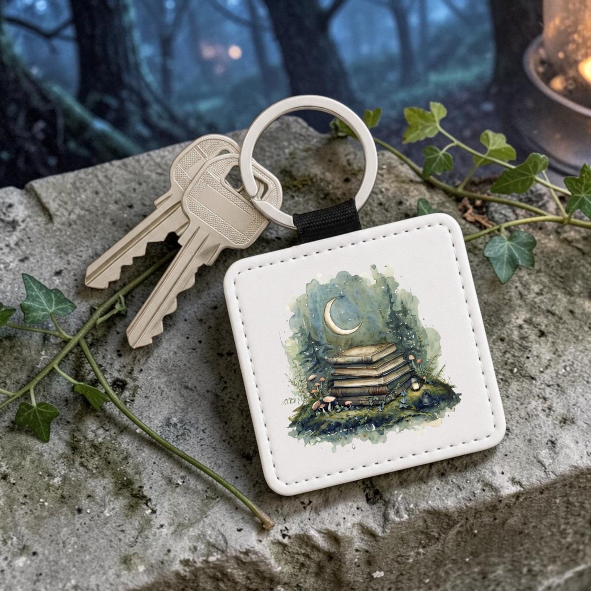 The Bookish Woodland Keychain by Mirabilia Boutique features enchanting art of books, a crescent moon, and tiny mushrooms on the keychain, alongside two keys resting on a stone. In the misty forest background, ivy leaves and a glowing lantern enhance its woodland charm—making it the perfect cottagecore accessory for any book lover.