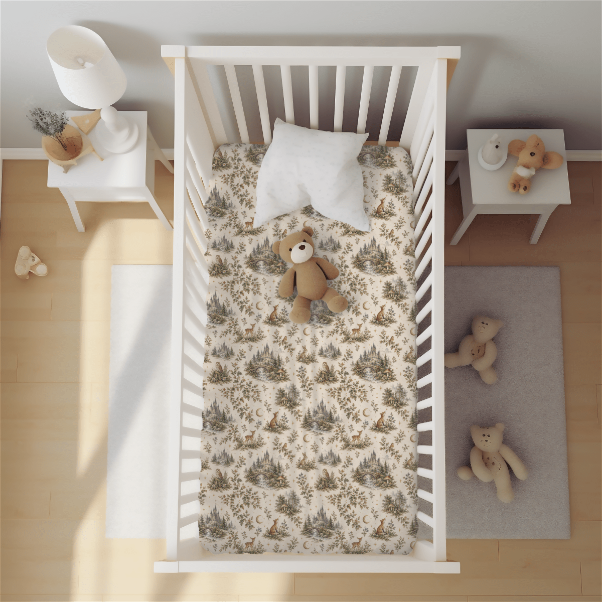 A crib featuring the Mirabilia Boutique Enchanted Woodlands Crib Sheet by Moon & Moss Nursery, styled with coordinating woodland bedding, a plush pillow, and a teddy bear inside. Beside the crib sits a small table adorned with a lamp and decorative accents. A cozy rug displays two teddy bears, while a pair of baby shoes rests on the floor—all captured from above in a bright, well-lit room.