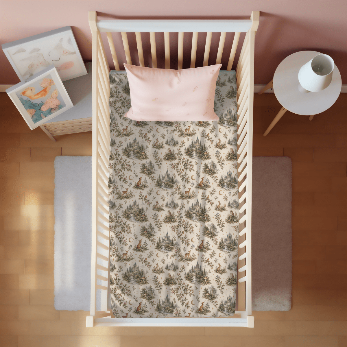 A top-down view of a crib featuring the Enchanted Woodlands Crib Sheet by Mirabilia Boutique and a pink pillow, placed beside a small round table with a vase and a soft rug on wooden flooring. Nursery wall art is visible nearby.