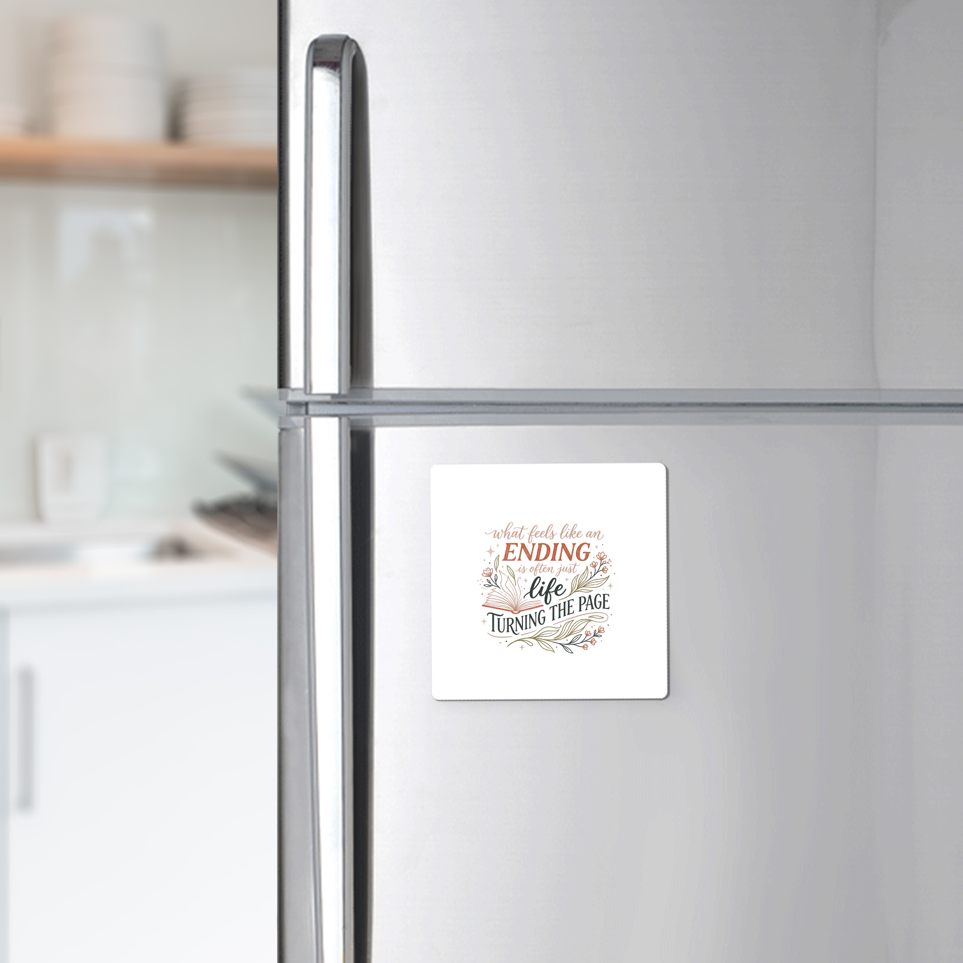 The Mirabilia Boutique Life Turning the Page Inspirational Magnet, a square fridge magnet with an uplifting quote, is shown on a silver refrigerator in a modern kitchen.