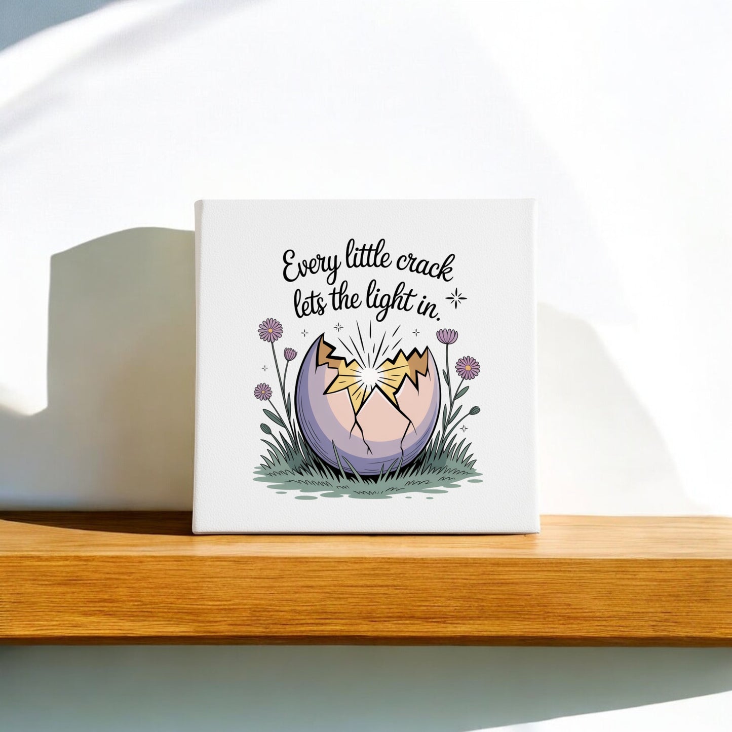 The Every Little Crack Lets the Light In Canvas Art by Mirabilia Boutique features a cracked egg with light shining through and flowers, plus the uplifting quote, making it perfect inspirational wall decor.