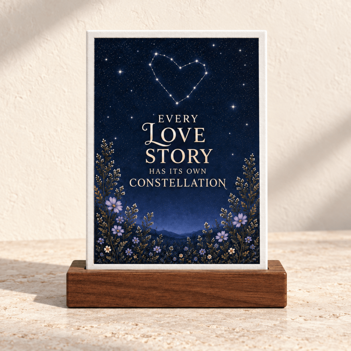 Every Love Story Constellation Mini Sign in a wooden base featuring a dark starry sky with a heart-shaped constellation and the text “Every love story has its own constellation” above purple flowers.