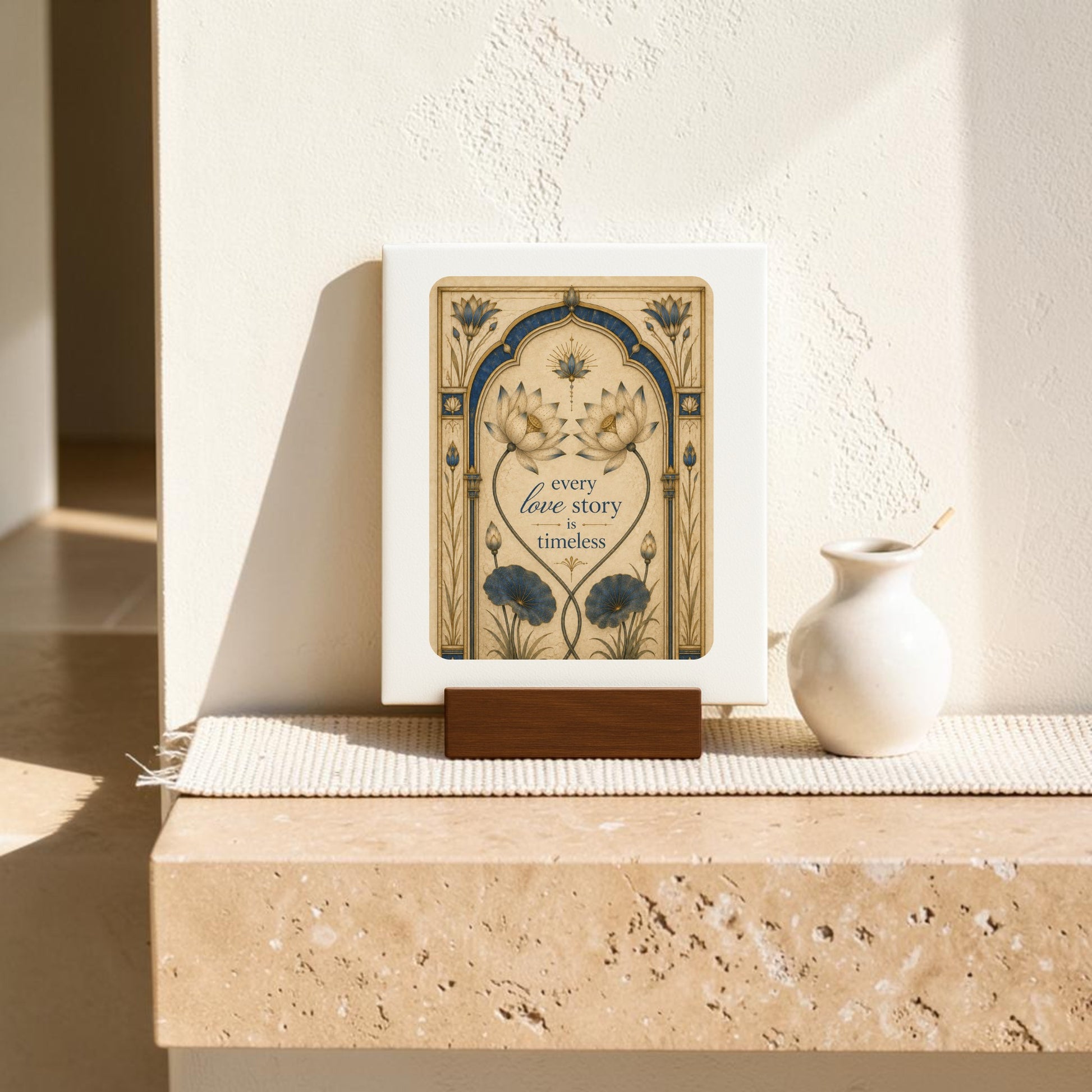 A framed art print from Mirabilia Boutique, the “Every Love Story Is Timeless | Lotus Mini Sign,” stands on a wooden base next to a small white vase, both part of the Lapis & Lotus Collection and displayed on a sunlit beige stone ledge.