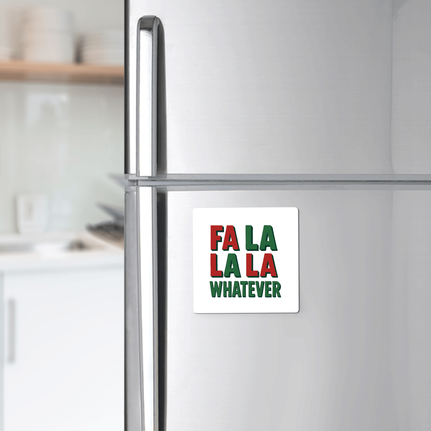 A silver refrigerator with the Mirabilia Boutique "Fa La La La Whatever" magnet—an amusing red, green, and white Christmas gift or stocking stuffer. Blurred kitchen in the background.