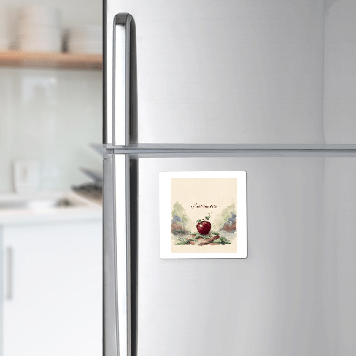 A silver refrigerator adorned with the Mirabilia Boutique "Just One Bite Fairy Tale Apple Magnet"—a square, handcrafted magnet featuring a red apple illustration and the phrase "Just one bite." The softly blurred kitchen background adds a whimsical cottagecore charm to your home décor.