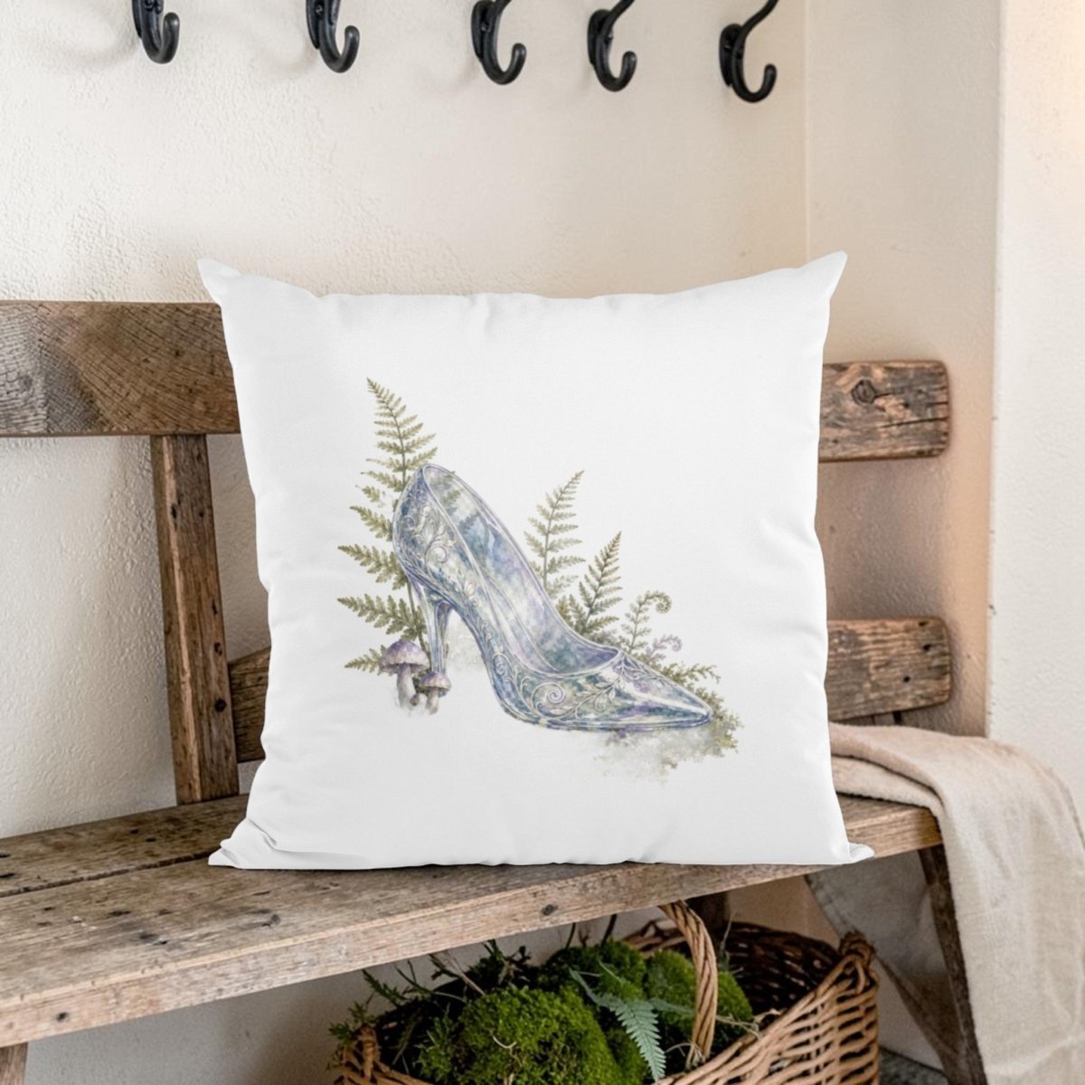 The Enchanted Glass Slipper Throw Pillow by Mirabilia Boutique rests on a rustic wooden bench, showcasing an illustration of a high-heeled shoe adorned with fern leaves and a tiny mushroom—bringing whimsical woodland charm and fairytale-inspired décor to your cozy farmhouse interior.
