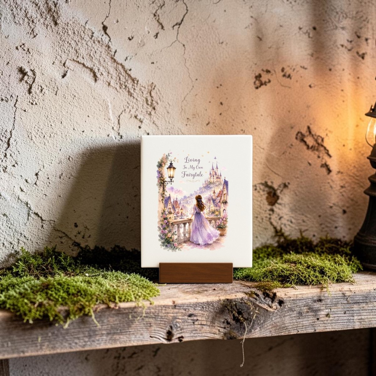 A “Living in My Own Fairytale Mini Canvas” by Mirabilia Boutique rests on a rustic, moss-covered wooden shelf. Surrounded by whimsical artwork that captures the enchanting spirit of cottagecore décor and softly illuminated by a warm lamp, its cover features a charming fairytale castle and princess beneath the title text, inviting you into an imaginative world.