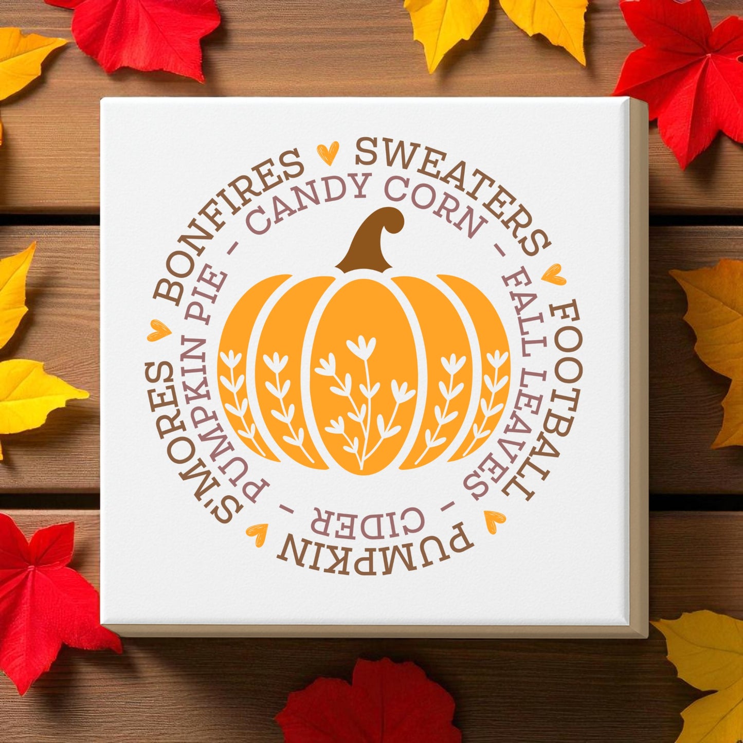The Fall Pumpkin Canvas by Mirabilia Boutique features an orange pumpkin and autumn words on a white 8x8 square, accented with colorful leaves—perfect cozy autumn wall art for your home decor.