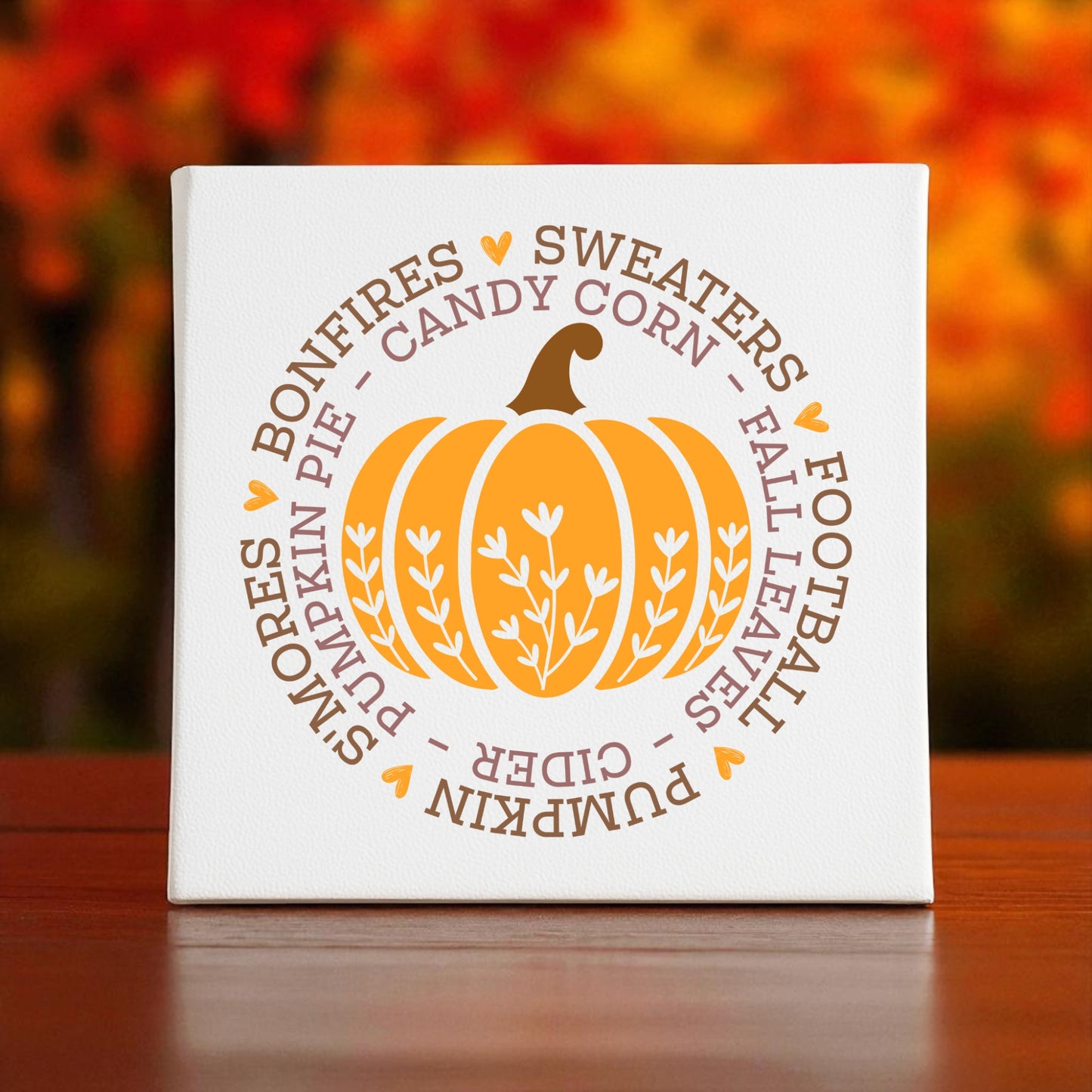 The Fall Pumpkin Canvas by Mirabilia Boutique is an 8x8 white wall art featuring an orange pumpkin, autumn words, and hearts—a cozy decor piece to warm up your space for autumn.