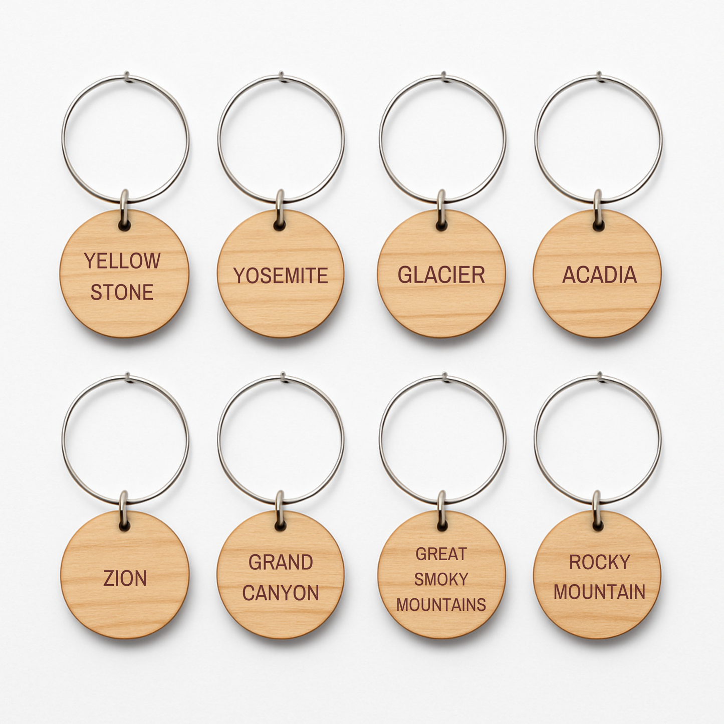 Set of eight round wooden keychains with metal rings by Mirabilia Boutique, each engraved with a national park—ideal for your parks collection or as unique "Favorite National Parks Wine Charms.