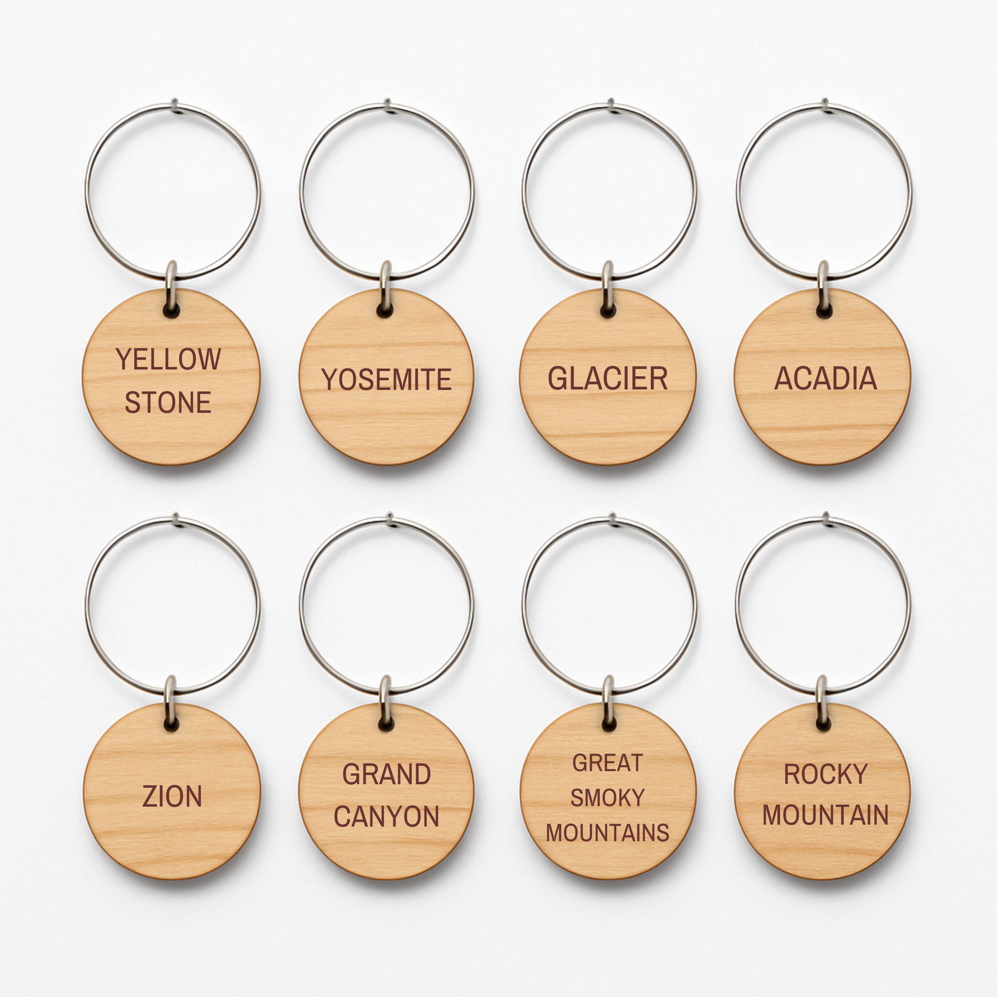 Set of eight round wooden keychains with metal rings by Mirabilia Boutique, each engraved with a national park—ideal for your parks collection or as unique "Favorite National Parks Wine Charms.