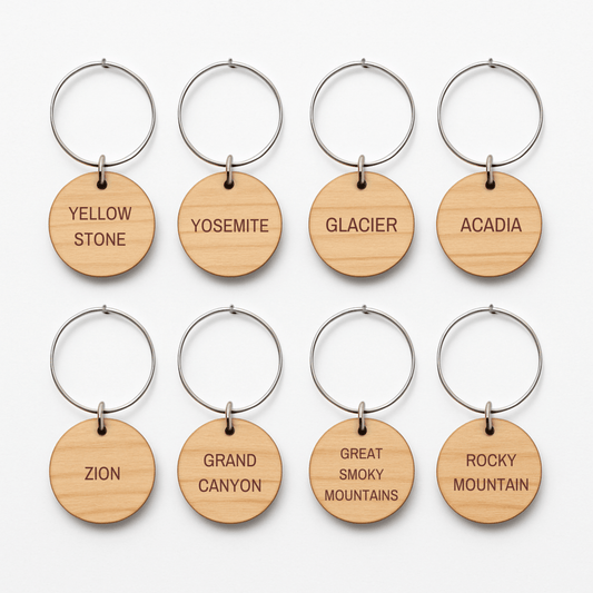 Set of eight round wooden keychains with metal rings by Mirabilia Boutique, each engraved with a national park—ideal for your parks collection or as unique "Favorite National Parks Wine Charms.