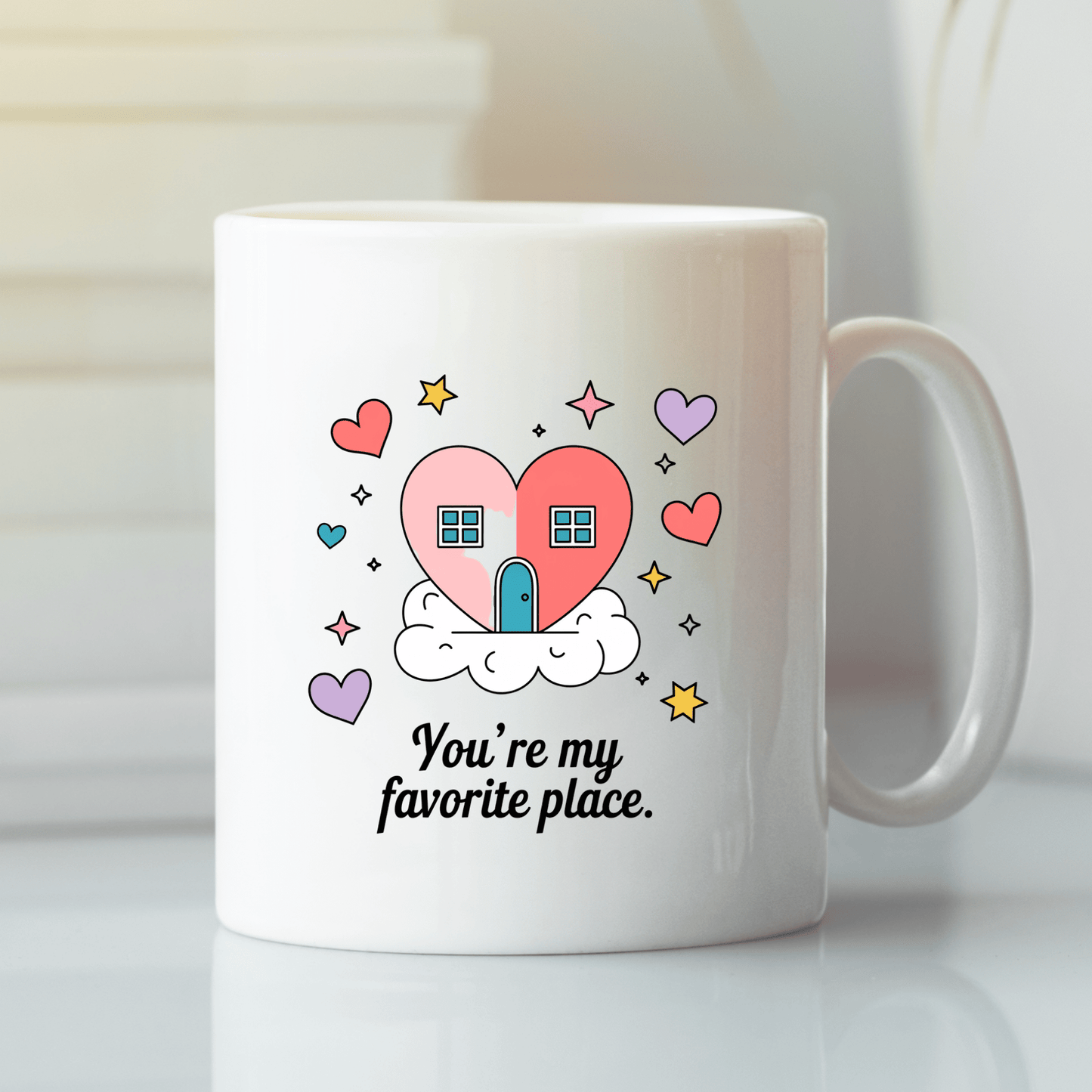 The Heart House Mug by Mirabilia Boutique features a pink heart-shaped house on a cloud with colorful hearts and stars, plus the phrase “You’re my favorite place.” A charming gift mug for someone special.