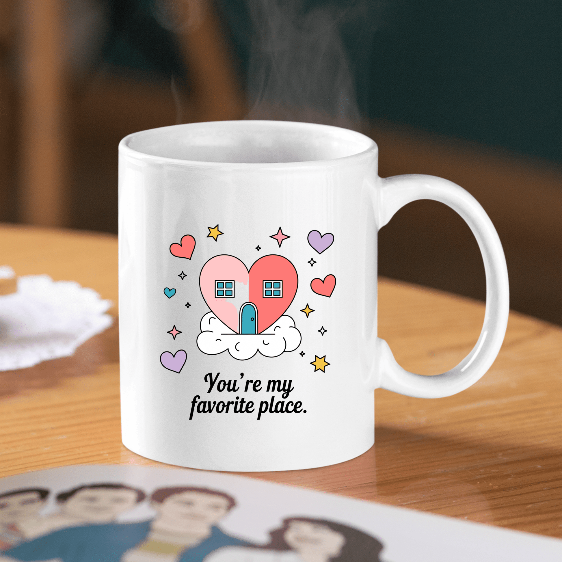 The Heart House Mug by Mirabilia Boutique features a heart-shaped house, colorful hearts, and clouds with the phrase "You're my favorite place," making it the perfect gift mug for someone special.