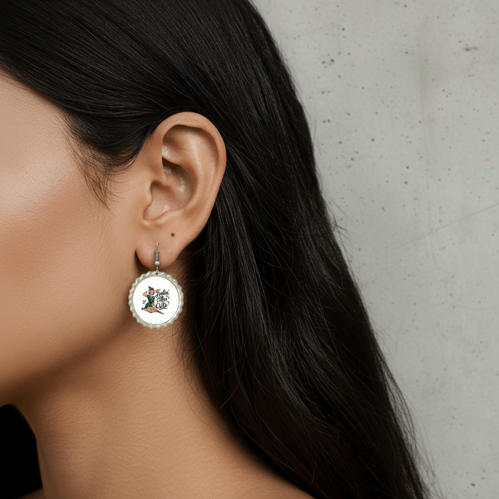 A woman with long dark hair wears Mirabilia Boutique's Feelin’ Elfin’ Cute Earrings, festive holiday jewelry for women, featuring a colorful bird and text. Only the left side of her face and ear are visible against a light gray background.