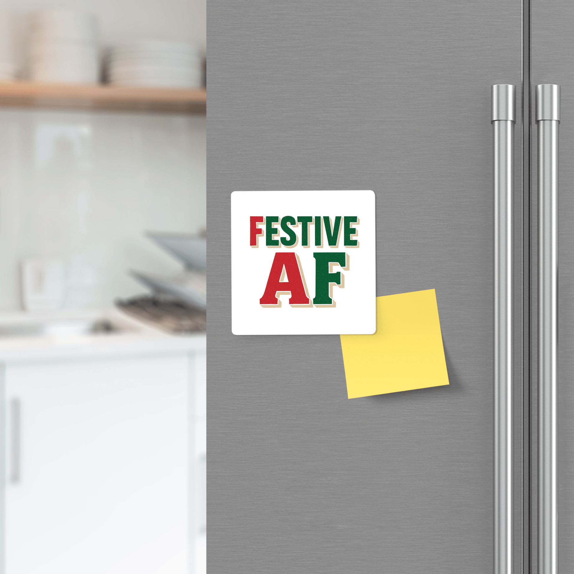 A Festive AF Magnet by Mirabilia Boutique, featuring green and red lettering, stands out on a kitchen fridge—a fun holiday decor gift or stocking stuffer—while a yellow sticky note and blurred kitchen backdrop enhance the Christmas vibe.