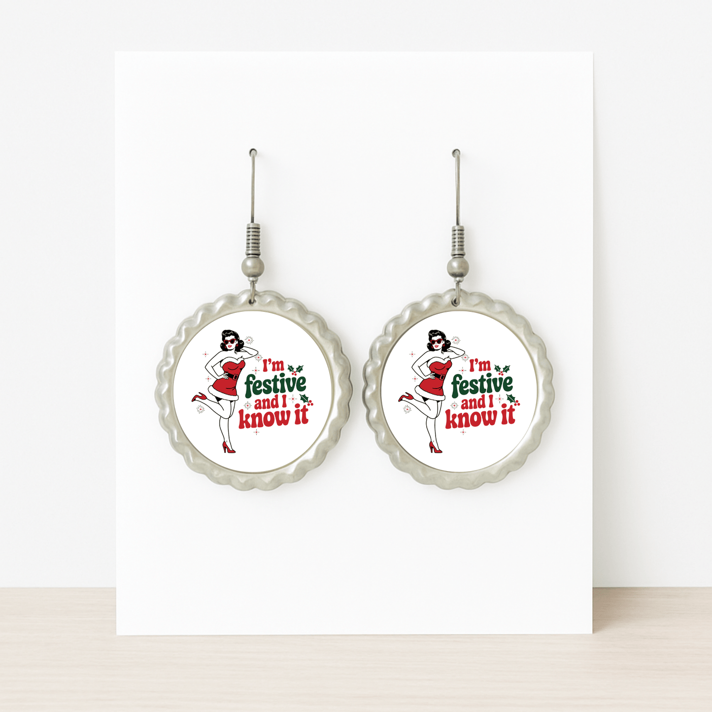 The Festive and I Know It Earrings by Mirabilia Boutique feature a retro pin-up girl in a Santa hat and red dress with "I'm festive and I know it" text, displayed on a white card—perfect for holiday flair.