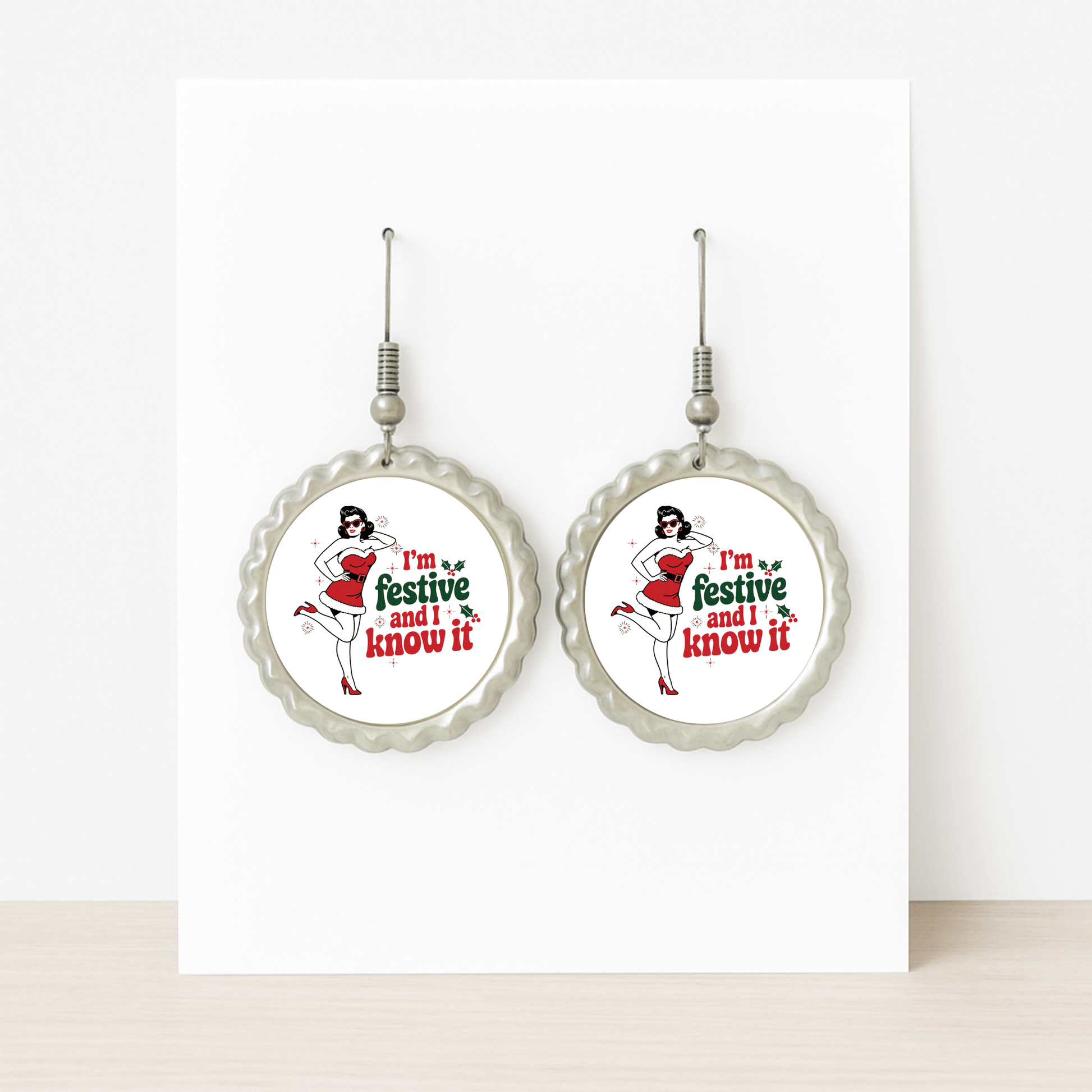 The Festive and I Know It Earrings by Mirabilia Boutique feature a retro pin-up girl in a Santa hat and red dress with "I'm festive and I know it" text, displayed on a white card—perfect for holiday flair.