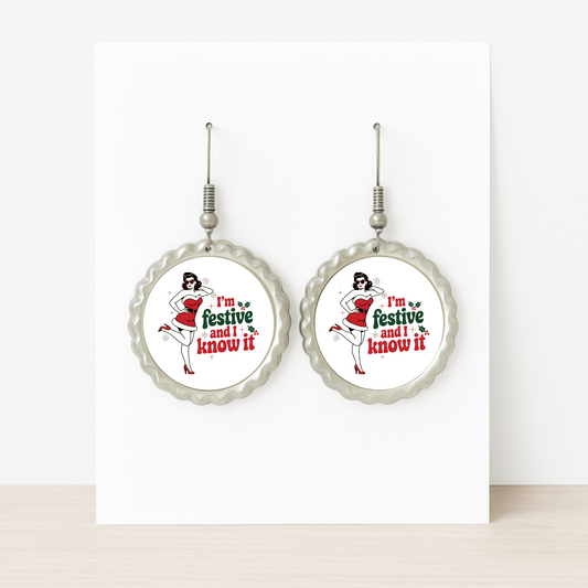 The Festive and I Know It Earrings by Mirabilia Boutique feature a retro pin-up girl in a Santa hat and red dress with "I'm festive and I know it" text, displayed on a white card—perfect for holiday flair.