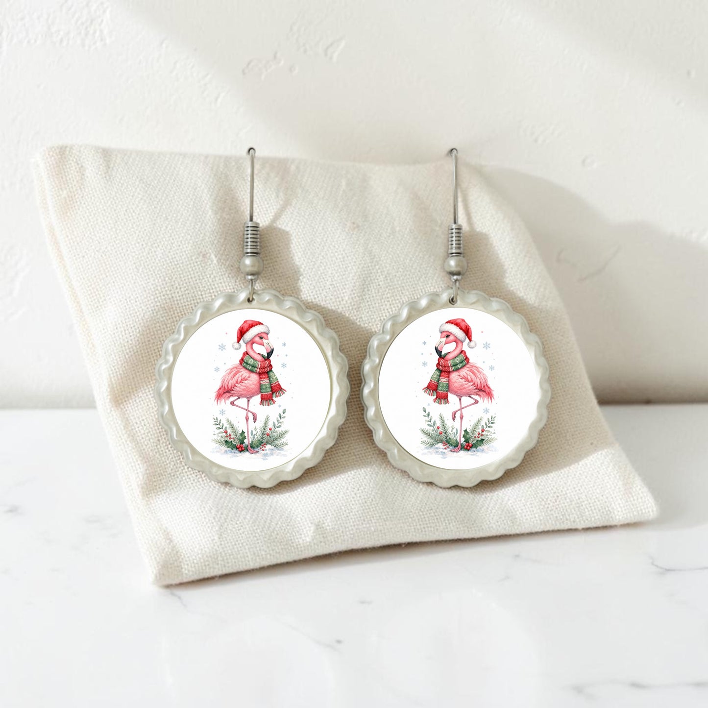 Add a playful holiday flair to your style with the Festive Flamingo Earrings | Winter Bird Jewelry from Mirabilia Boutique. This handcrafted pair features round earrings depicting flamingos in Santa hats and scarves, beautifully displayed on a cream fabric pouch against a white background—perfect for bringing fun Christmas spirit to any look.