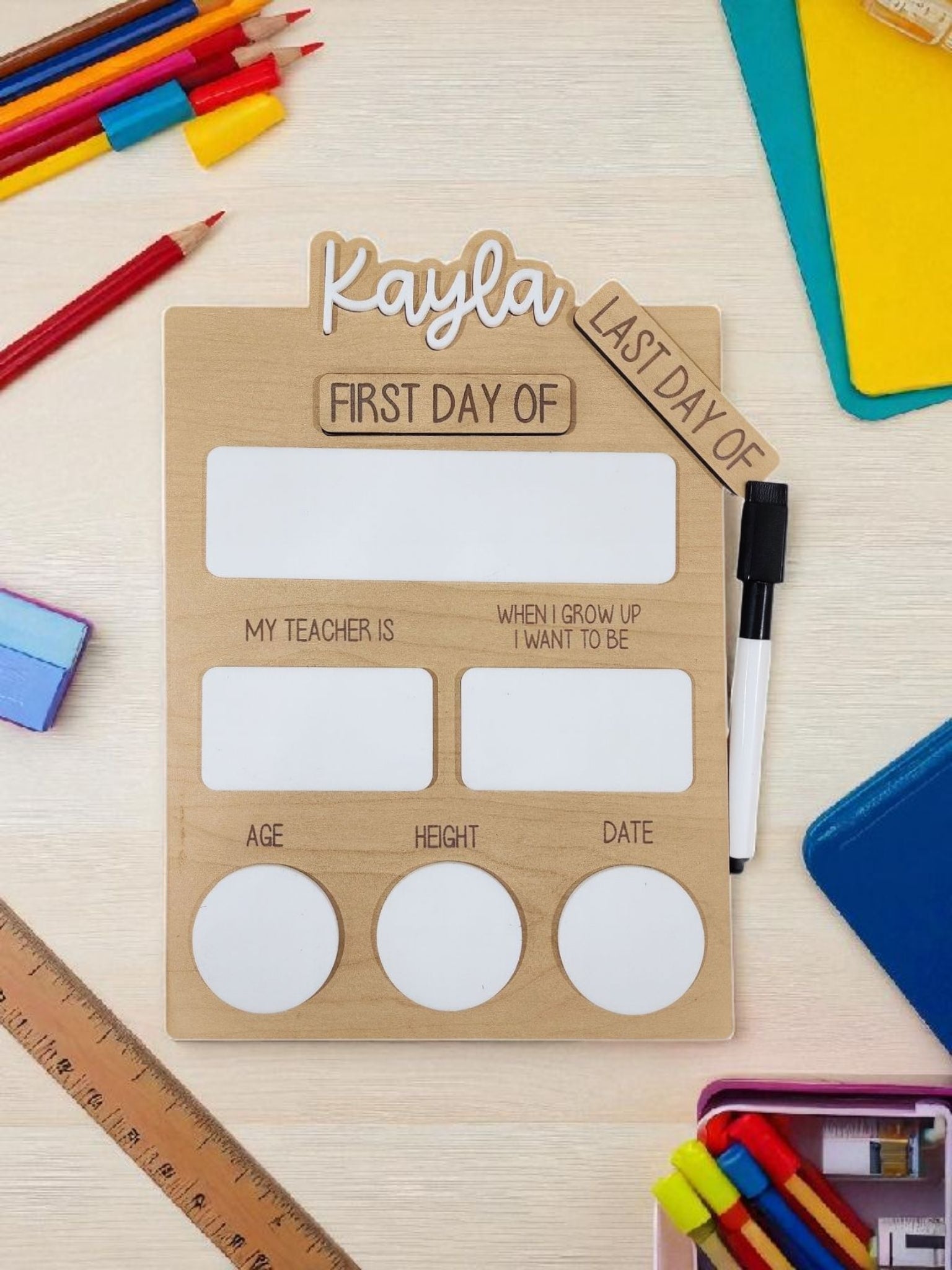 The Mirabilia Boutique Reusable School Board is a dry-erase First & Last Day of School Sign with spaces for name, teacher, aspiration, age, height, and date—ideal for memorable school photos. Dry erase marker included; decorated with colorful school supplies.