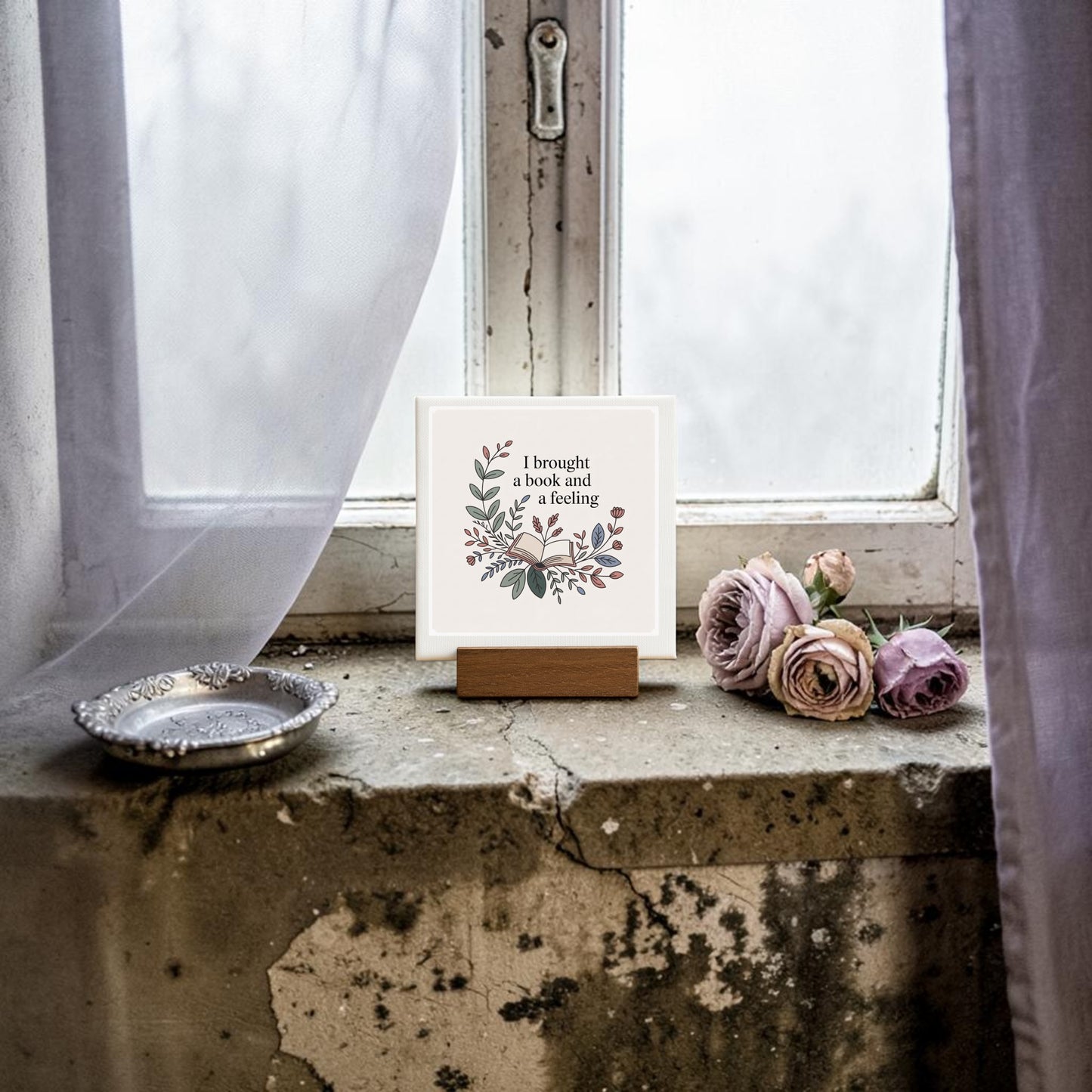 The “I Brought a Book and a Feeling” Mini Sign by Mirabilia Boutique rests on a rustic windowsill—ideal reading decor or book lover gift—beside soft pink roses, sheer curtains, and an antique silver dish.